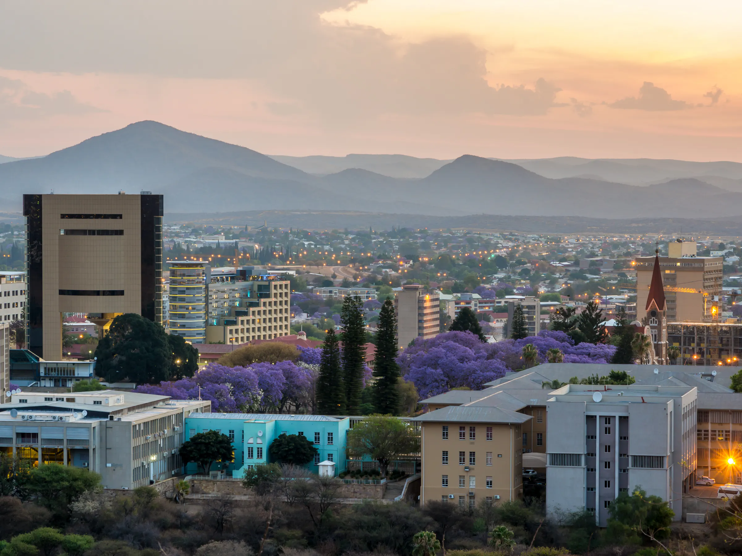 Windhoek's low-rise skyline and a red-roofed church spread across a wide valley under blue sky.