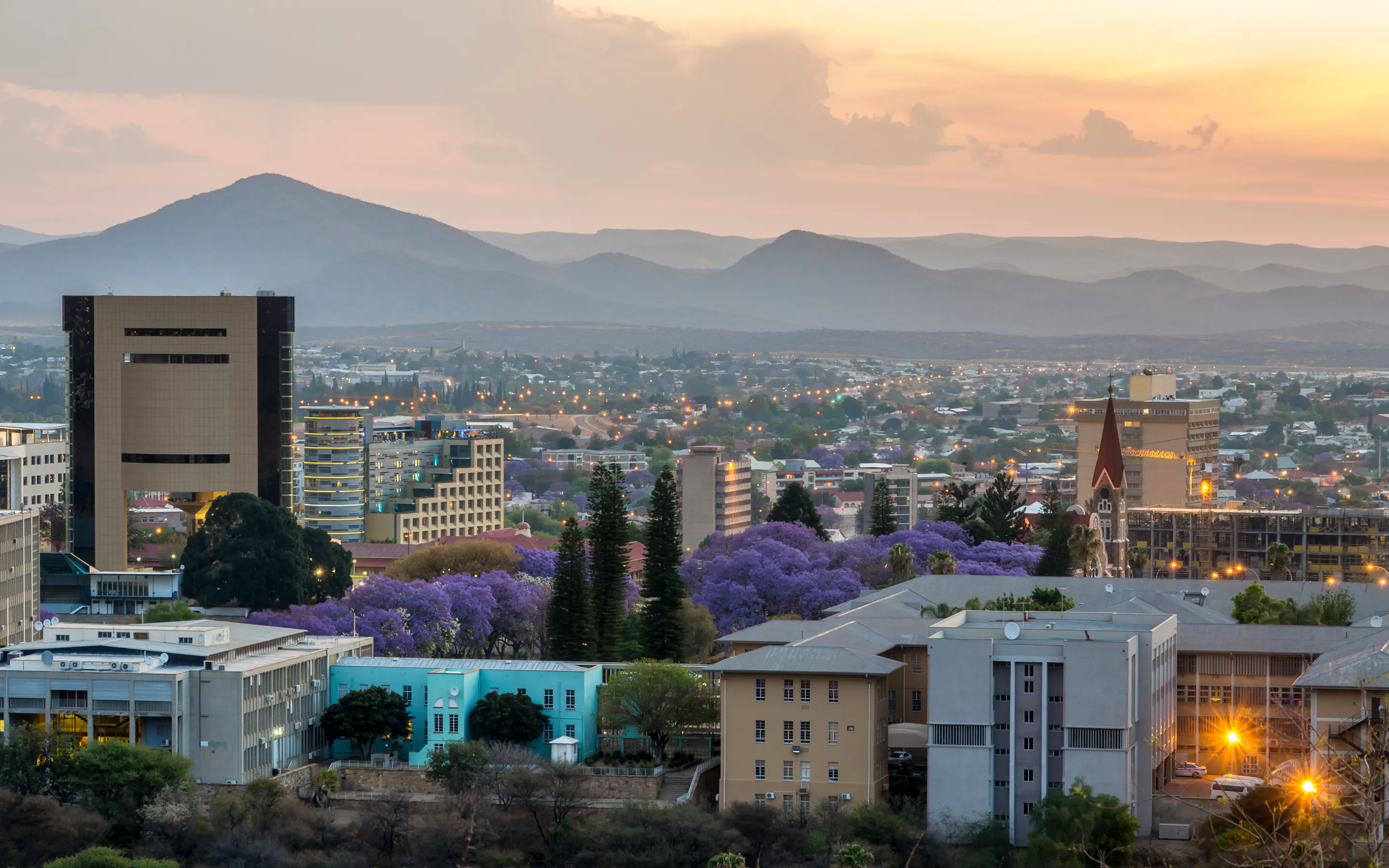 Windhoek's low-rise skyline and a red-roofed church spread across a wide valley under blue sky.