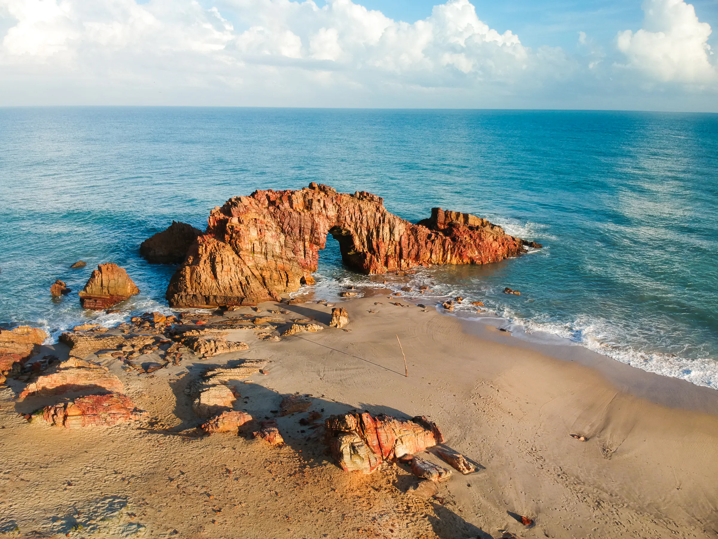 Rocky red boulders and small trees sit at the edge of a calm turquoise sea on Brazil's northeast coast.