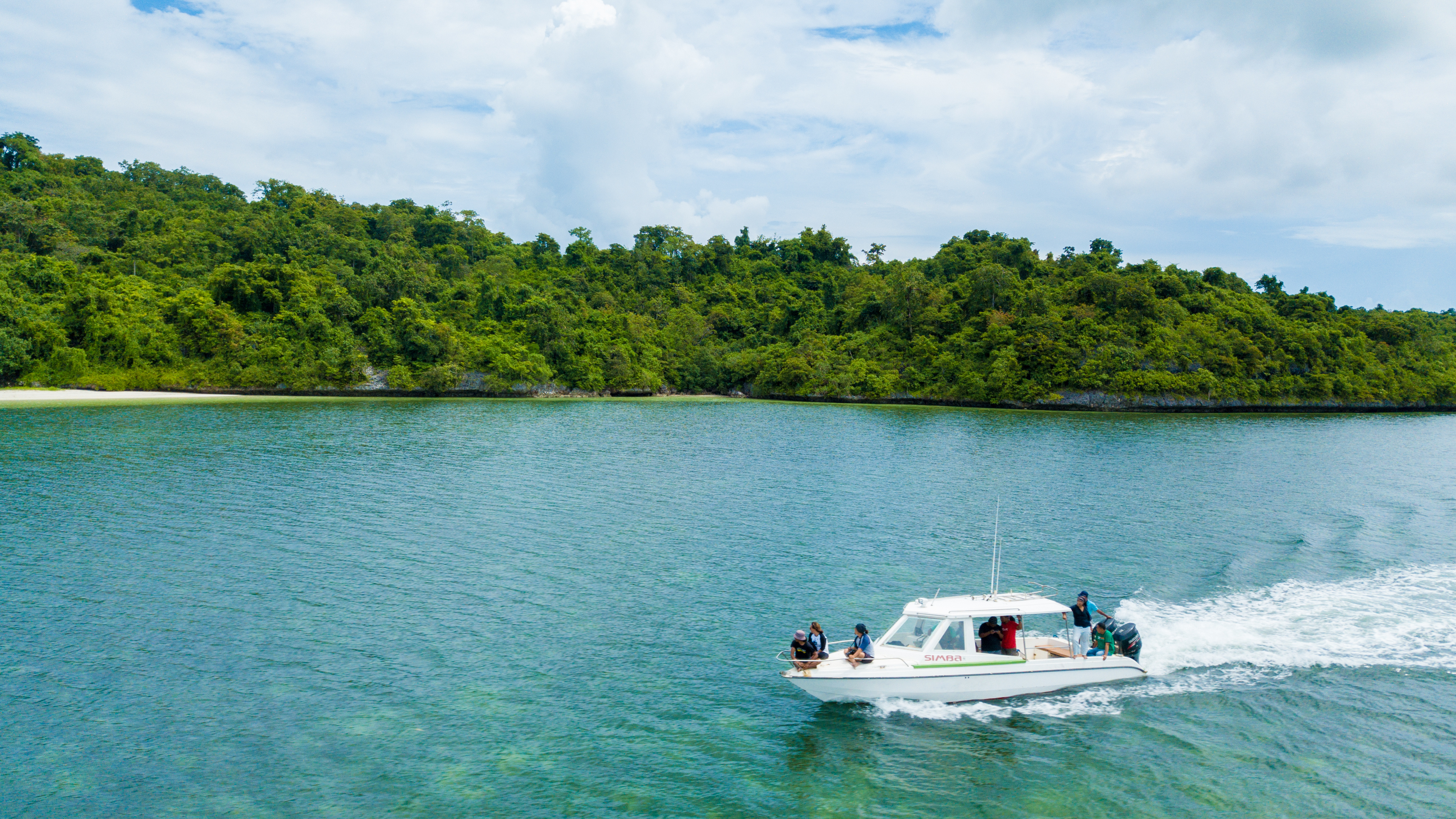 A motorboat speeds along a calm channel bordered by dense green rainforest in Sulawesi, Indonesia.