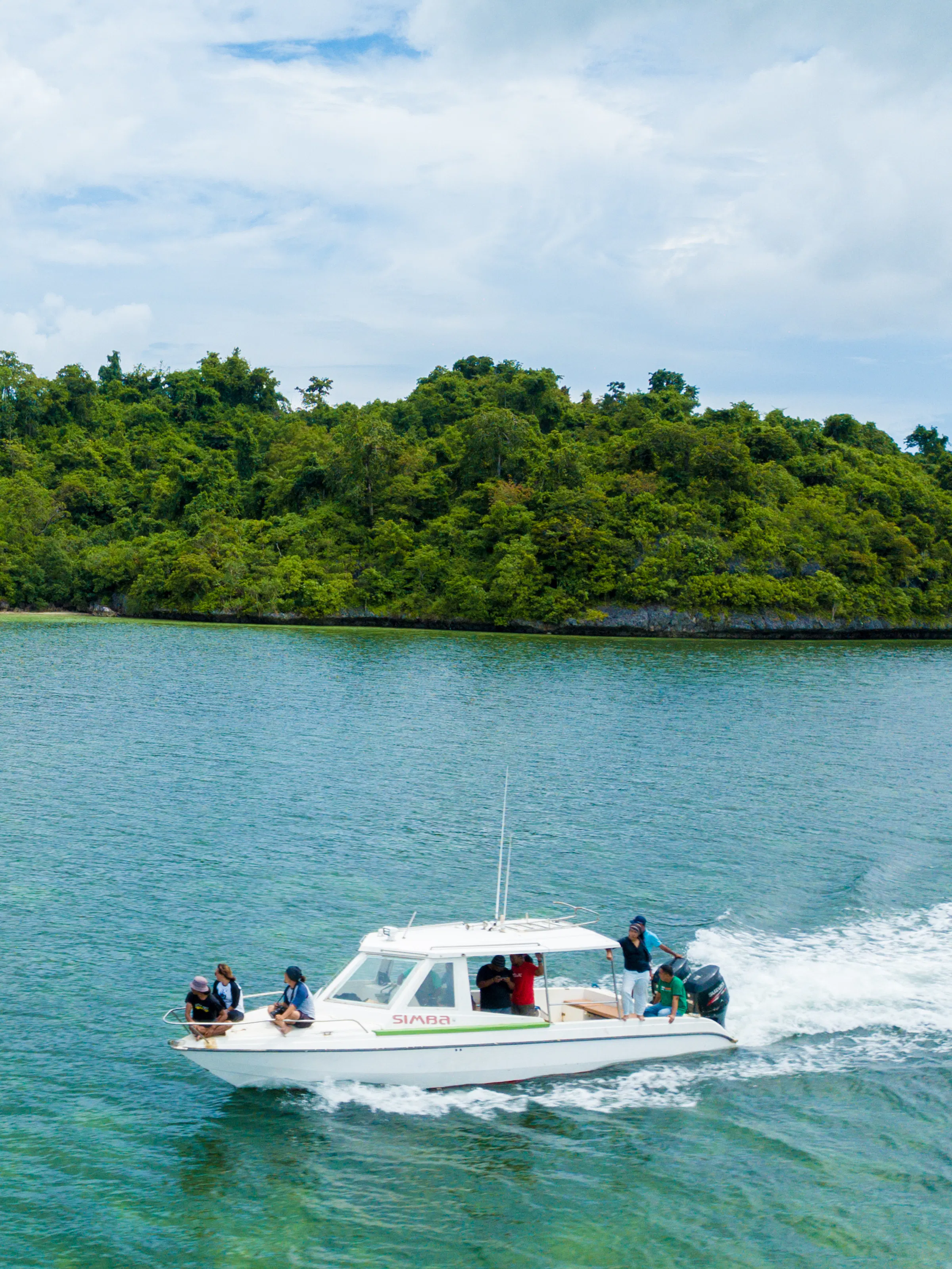 A motorboat speeds along a calm channel bordered by dense green rainforest in Sulawesi, Indonesia.