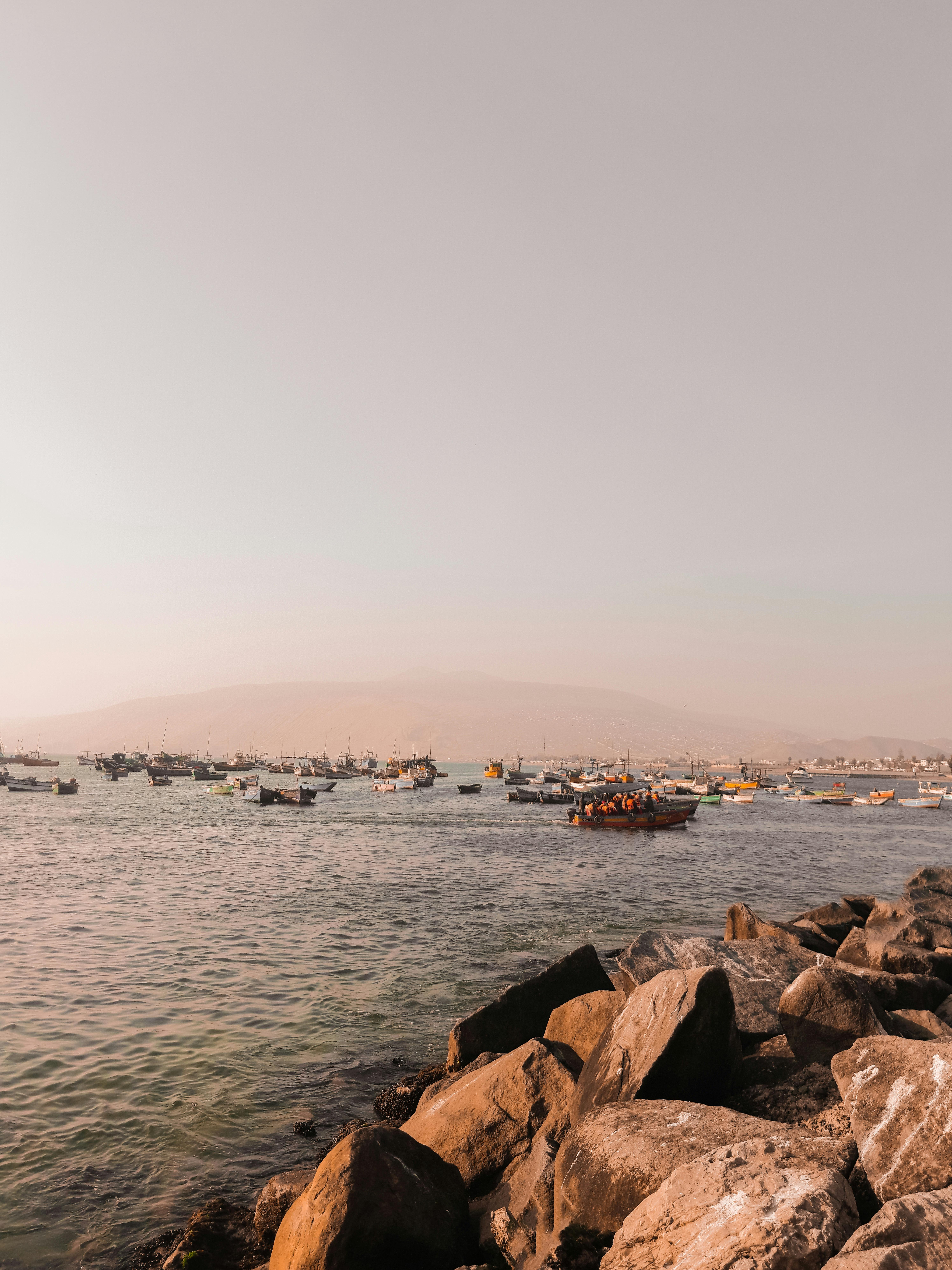 Rocky boulders line the Pacific shoreline at Lima with a hazy sky and calm grey sea beyond.