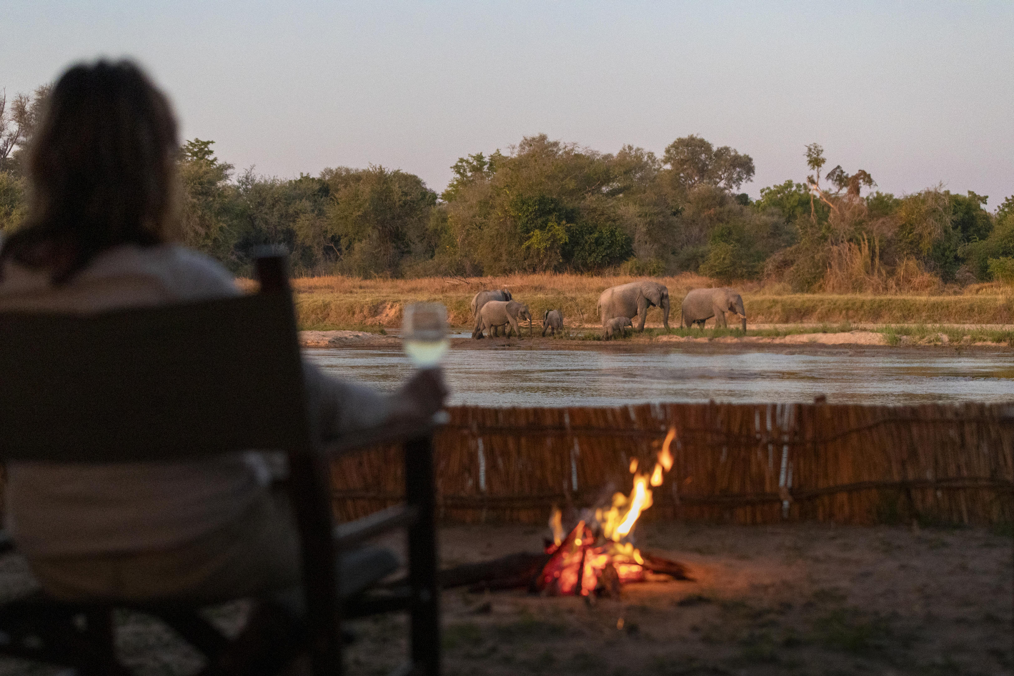 A campfire burns beside a simple wooden chair at a remote wilderness camp in North Luangwa.