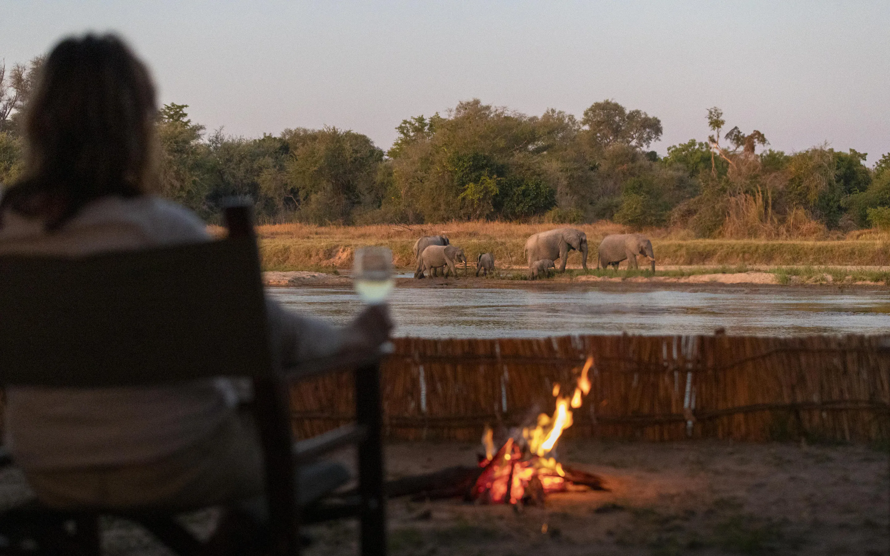 A campfire burns beside a simple wooden chair at a remote wilderness camp in North Luangwa.