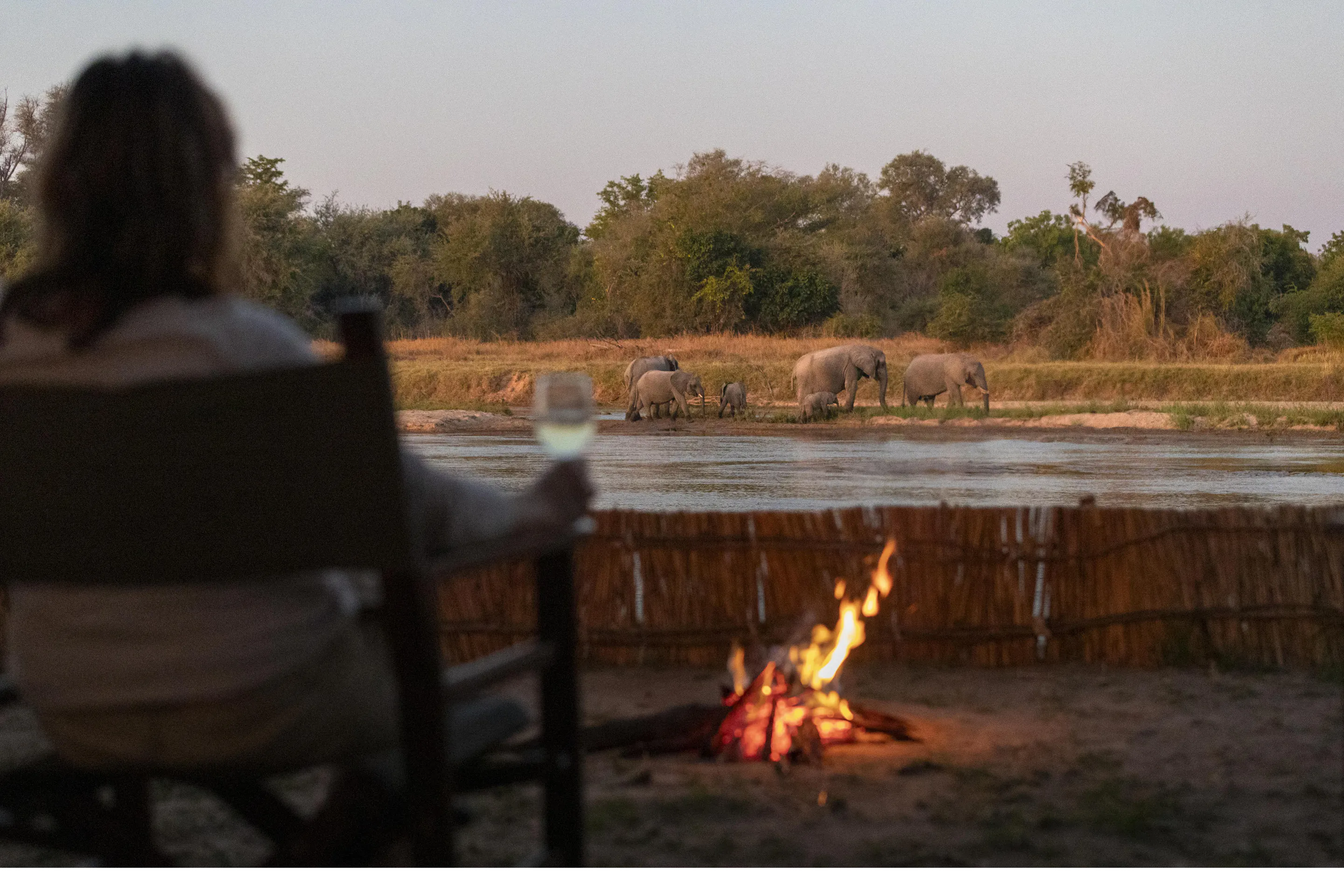 A campfire burns beside a simple wooden chair at a remote wilderness camp in North Luangwa.