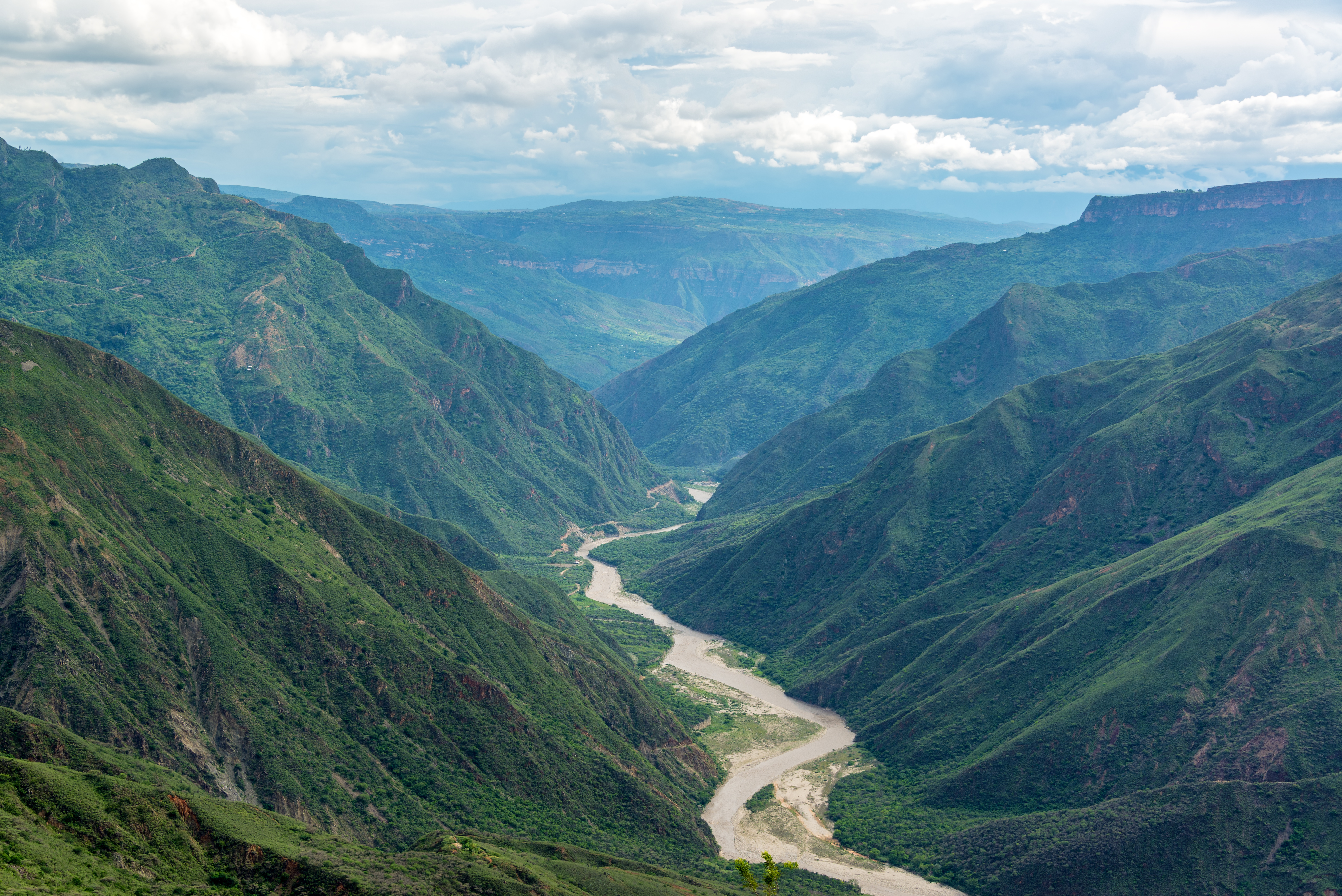 A broad green river valley winds between forested ridges as seen from Barichara, Colombia.