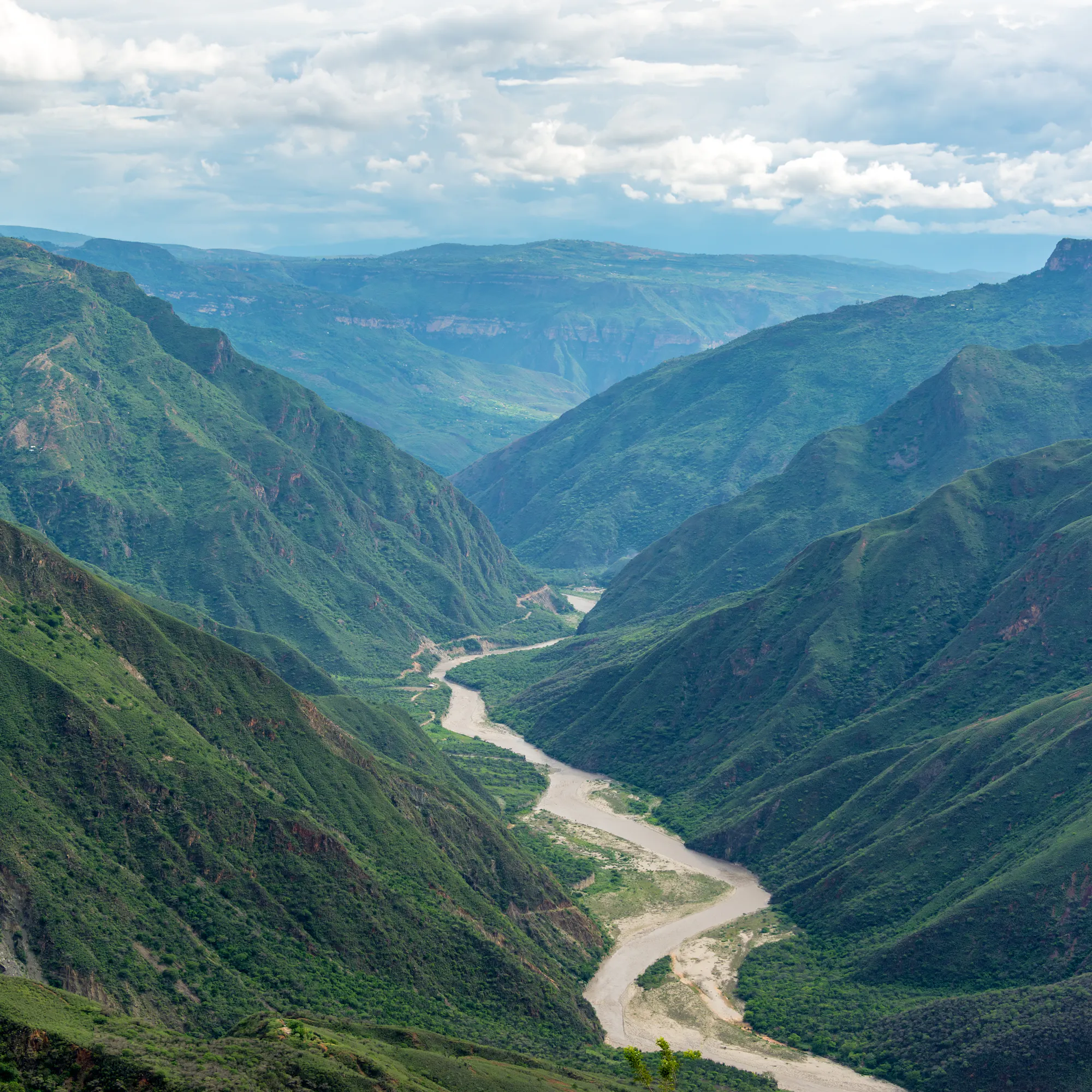 A broad green river valley winds between forested ridges as seen from Barichara, Colombia.
