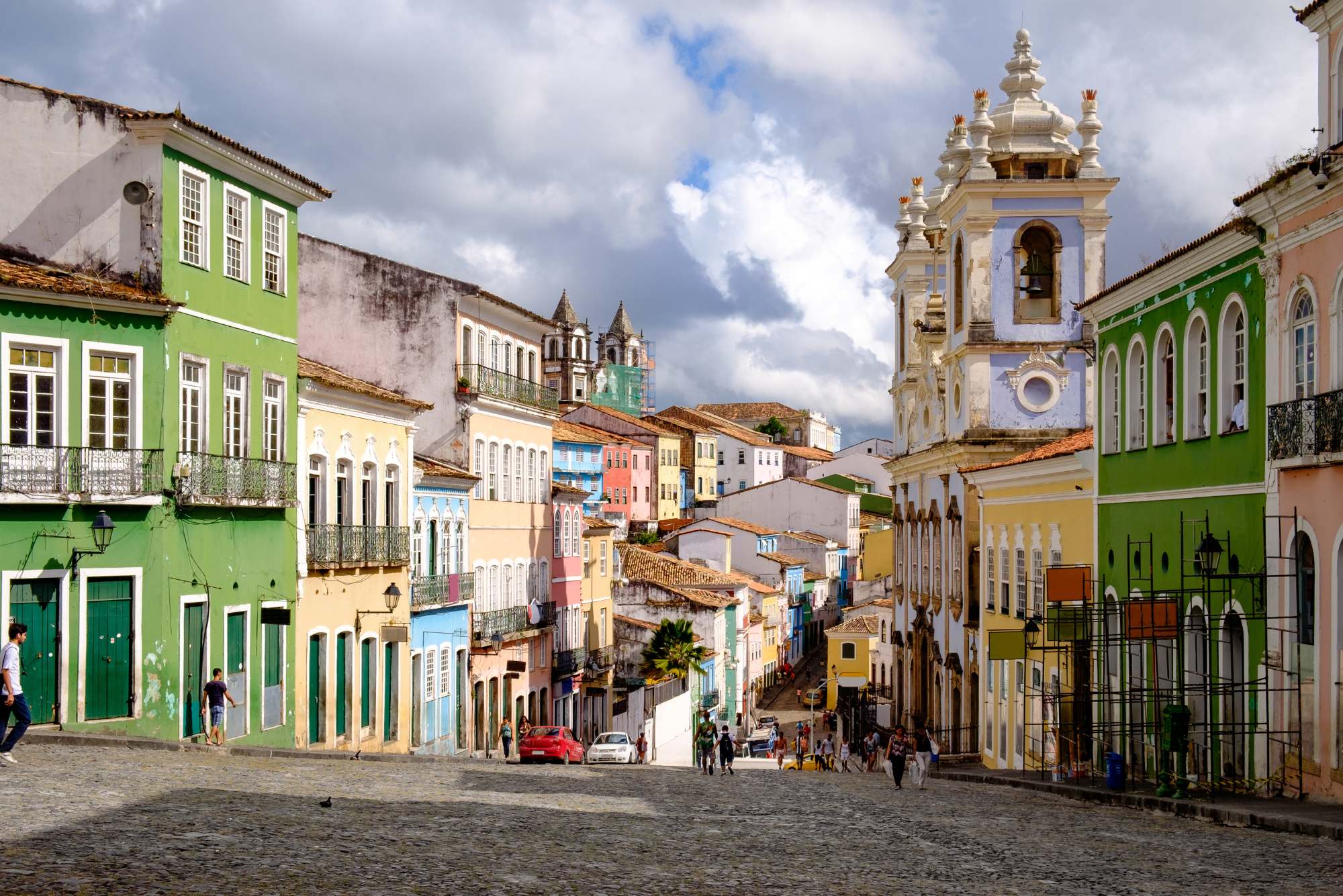 Colorful colonial buildings in shades of yellow and green line a cobblestone street in Salvador.