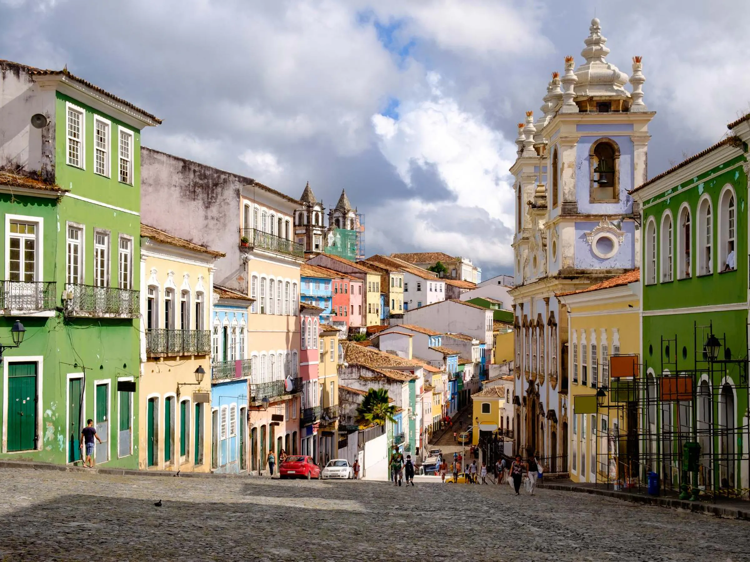 Colorful colonial buildings in shades of yellow and green line a cobblestone street in Salvador.