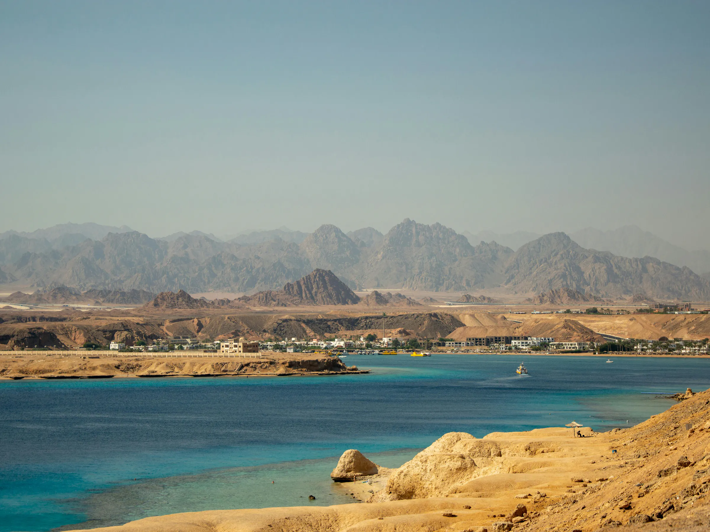 A scuba diver descends through clear blue water toward a coral reef in Egypt's Red Sea.