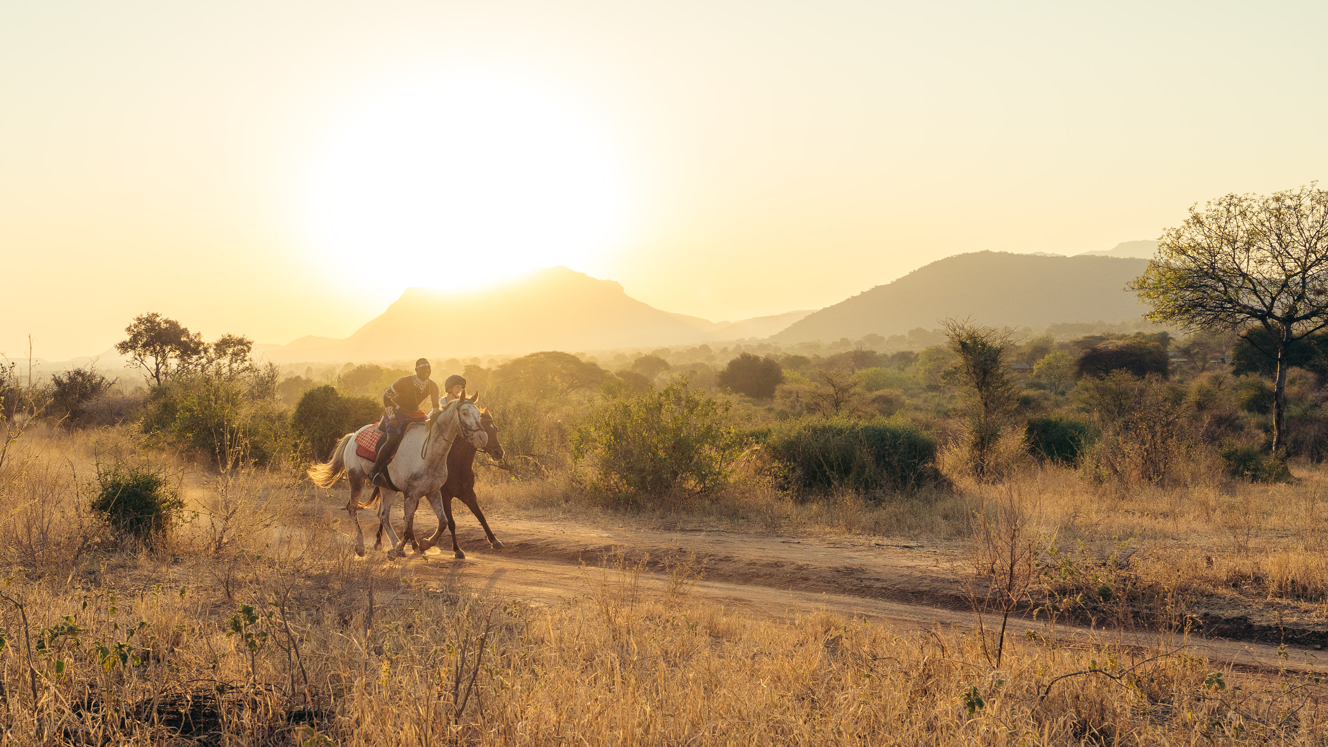 Riders on horseback move through open golden savanna beneath a wide sky in Kenya's Matthews Range.
