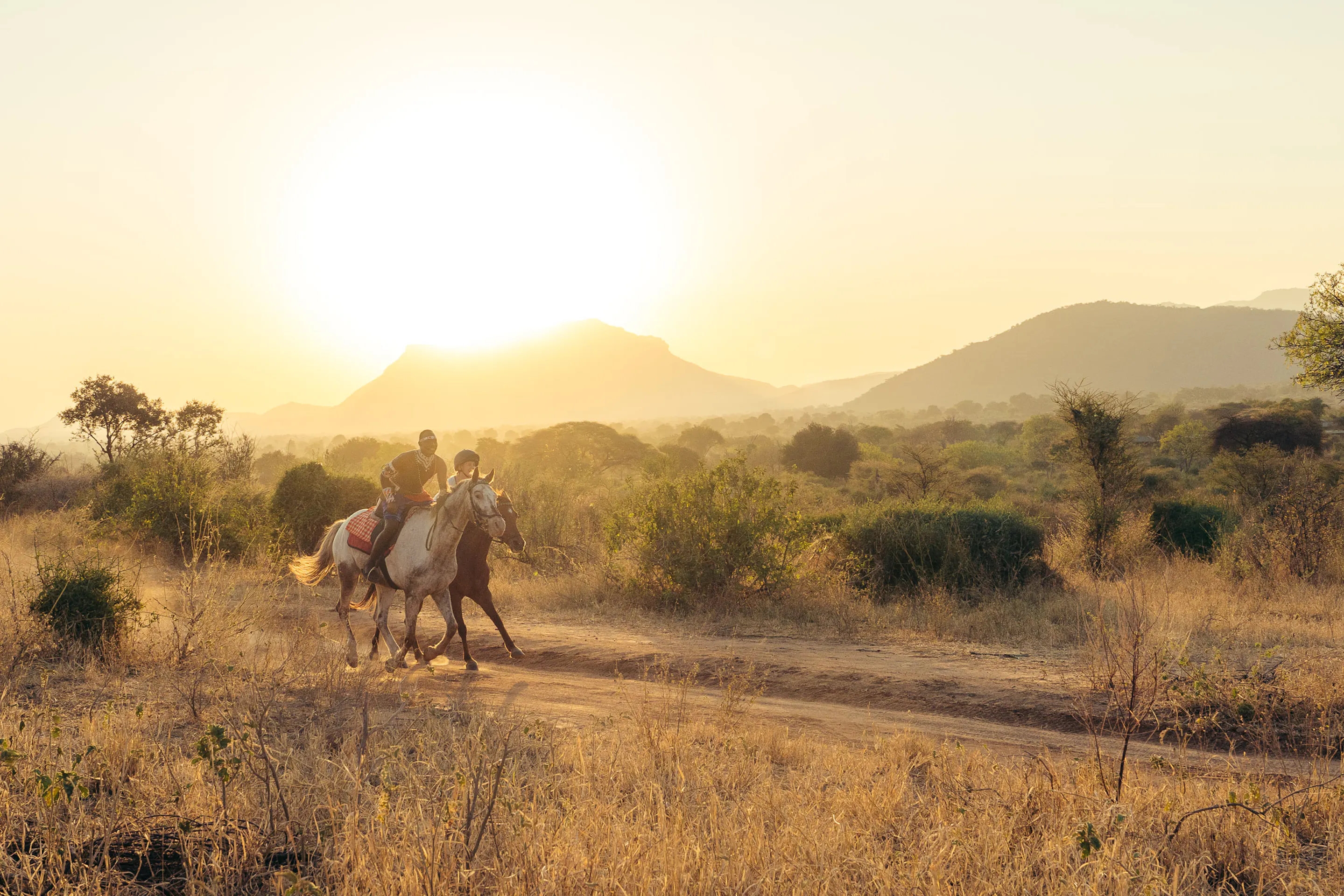Riders on horseback move through open golden savanna beneath a wide sky in Kenya's Matthews Range.