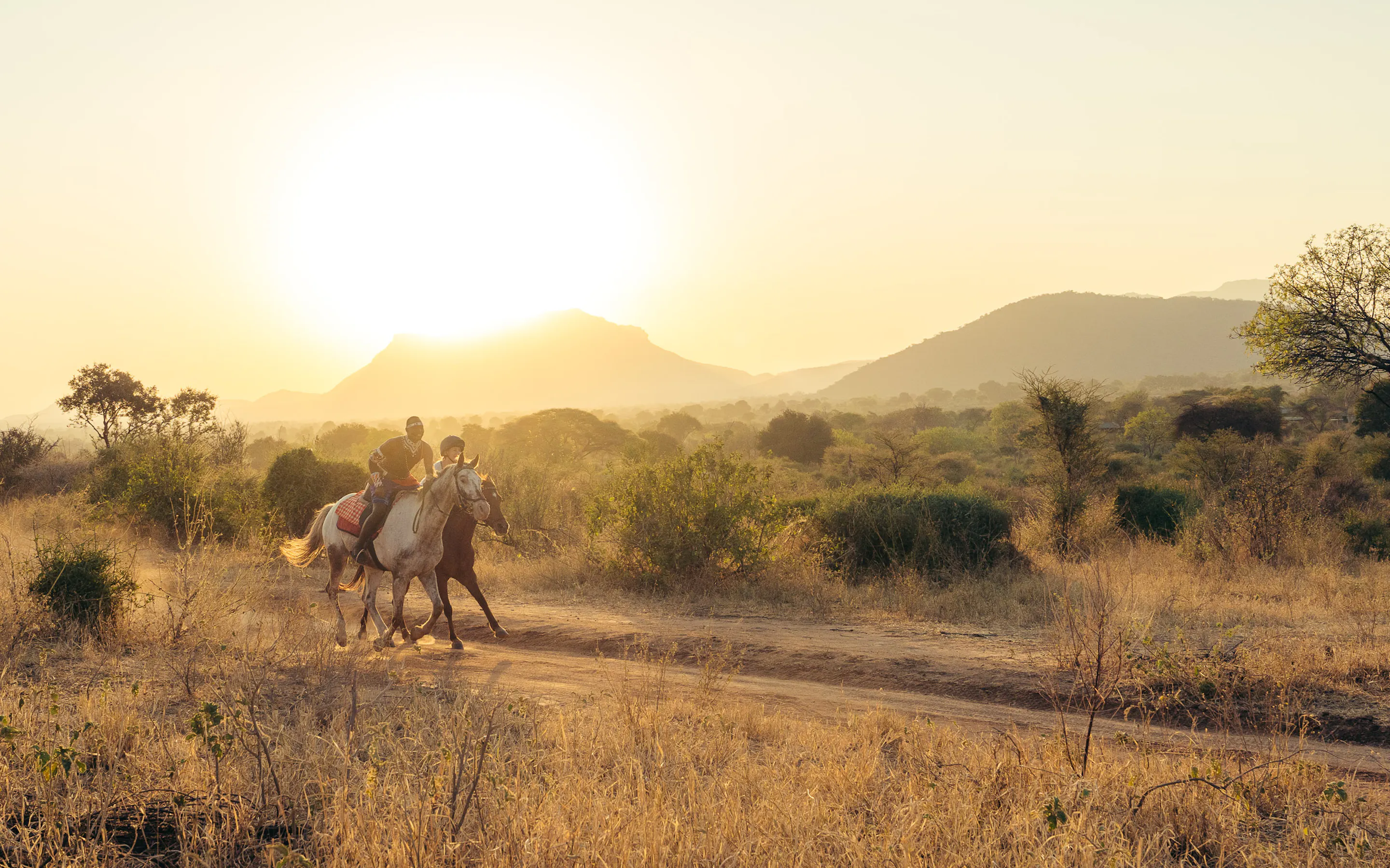 Riders on horseback move through open golden savanna beneath a wide sky in Kenya's Matthews Range.