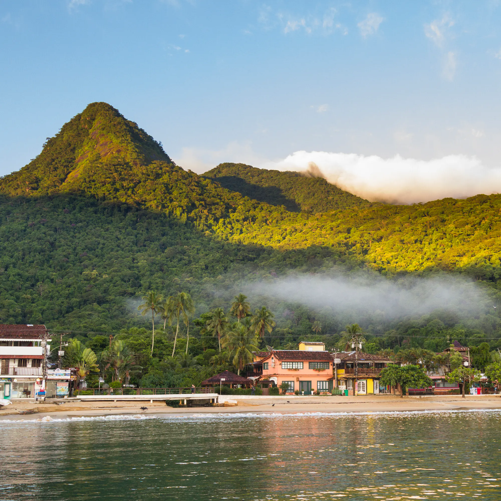 A densely forested green island rises sharply from the calm turquoise sea near Ilha Grande.