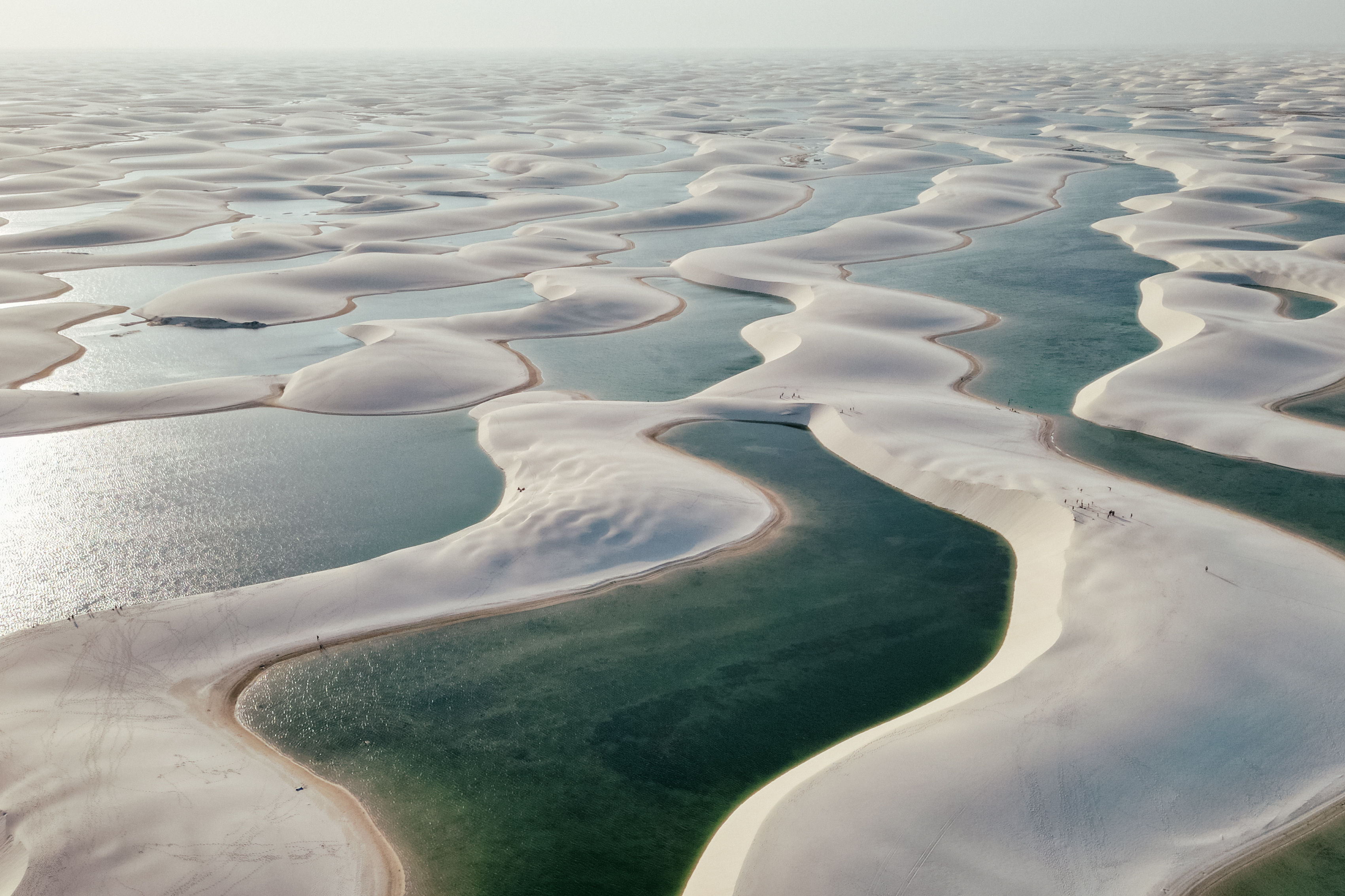 Aerial view of the Lençóis Maranhenses shows endless white dunes interspersed with blue lagoons.