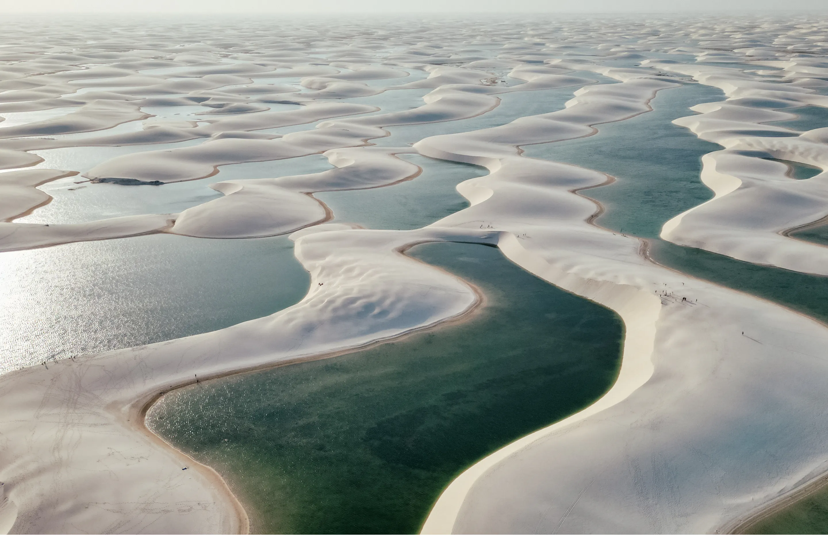 Aerial view of the Lençóis Maranhenses shows endless white dunes interspersed with blue lagoons.