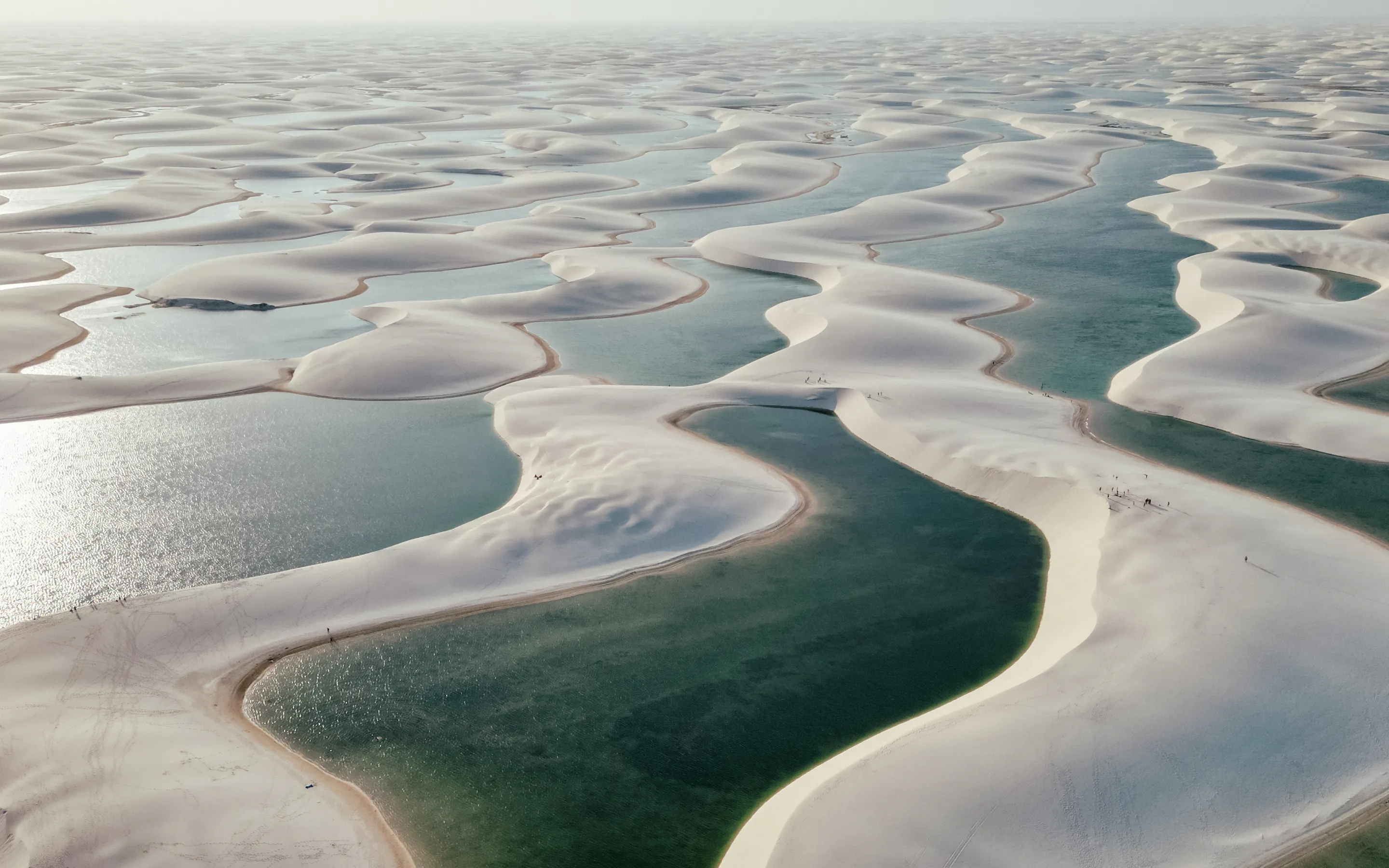 Aerial view of the Lençóis Maranhenses shows endless white dunes interspersed with blue lagoons.