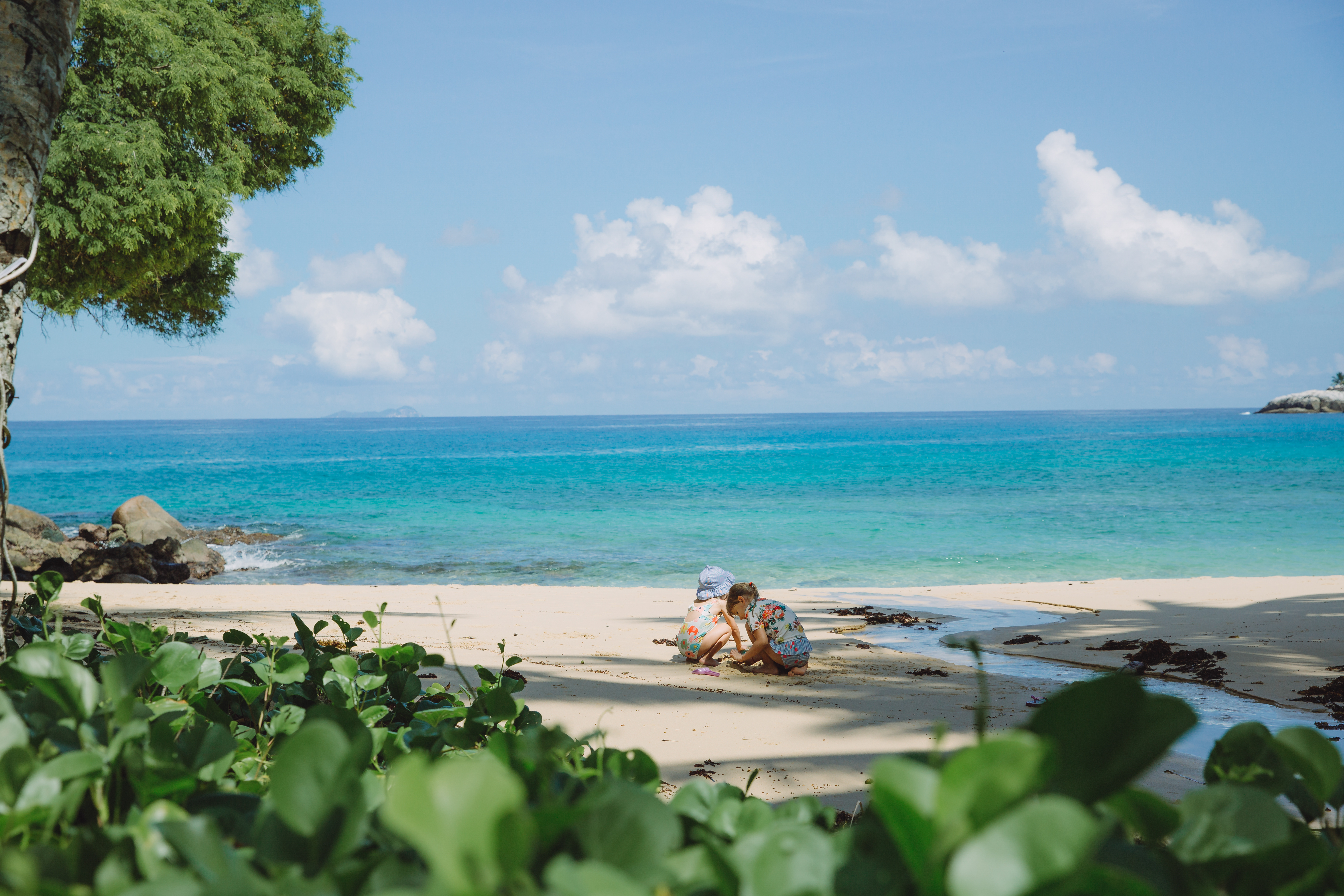 A sun lounger sits on a pristine white sand beach beside calm turquoise water in the Seychelles.