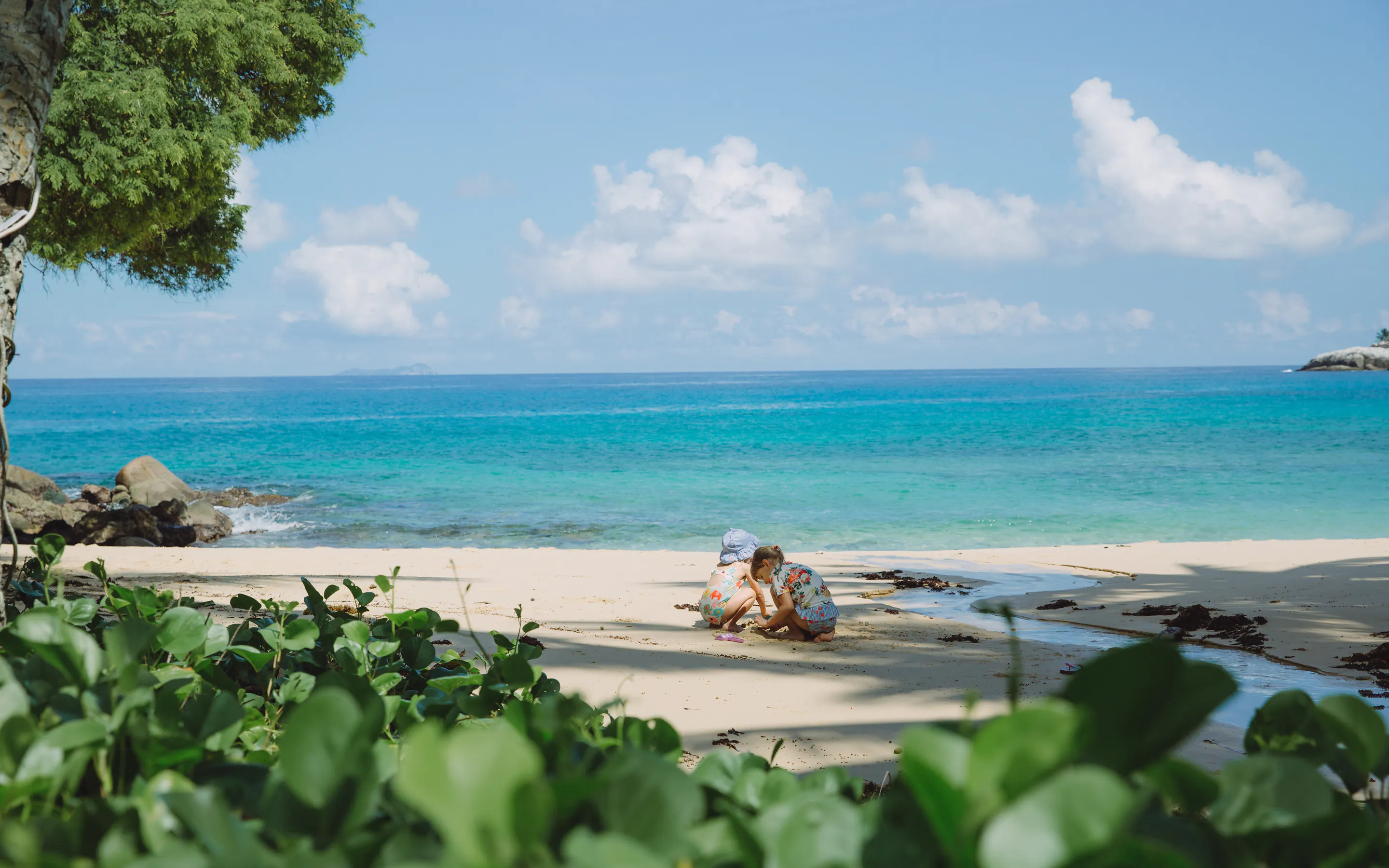 A sun lounger sits on a pristine white sand beach beside calm turquoise water in the Seychelles.