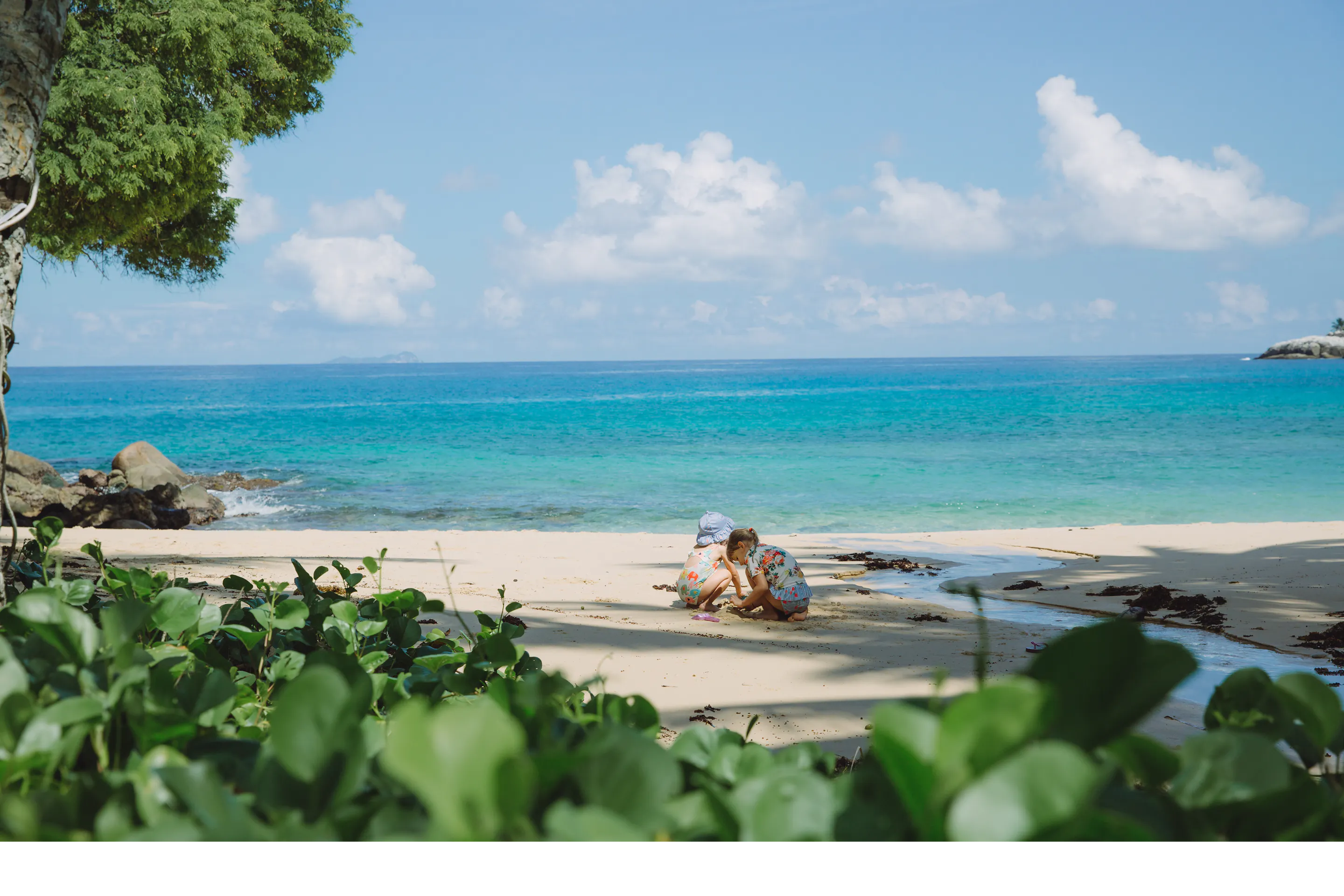 A sun lounger sits on a pristine white sand beach beside calm turquoise water in the Seychelles.