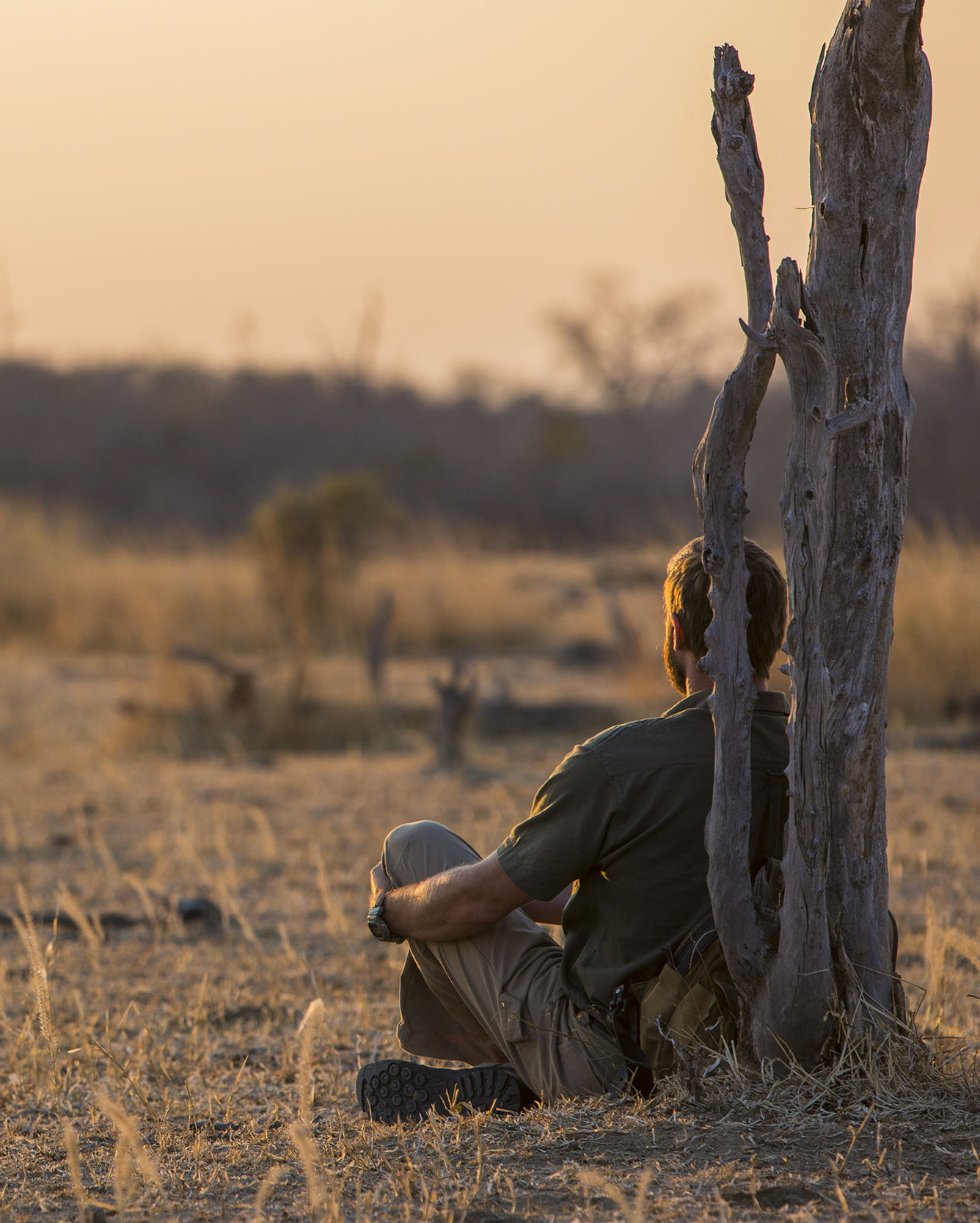 A man sits alone on a wooden chair at sunset overlooking a dry sandy riverbed in North Luangwa.