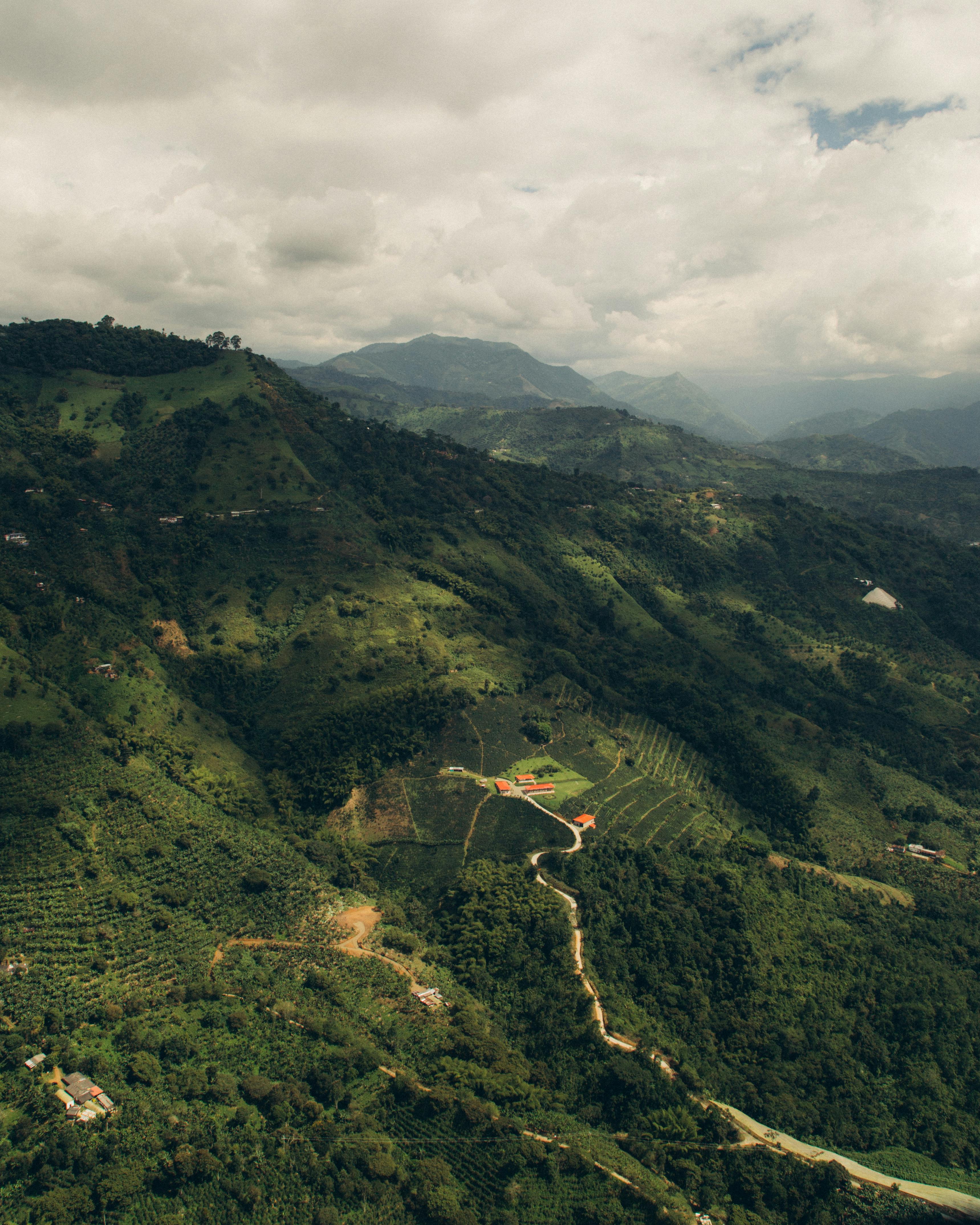 A lush green Colombian mountain valley with forested ridges recedes under overcast skies.