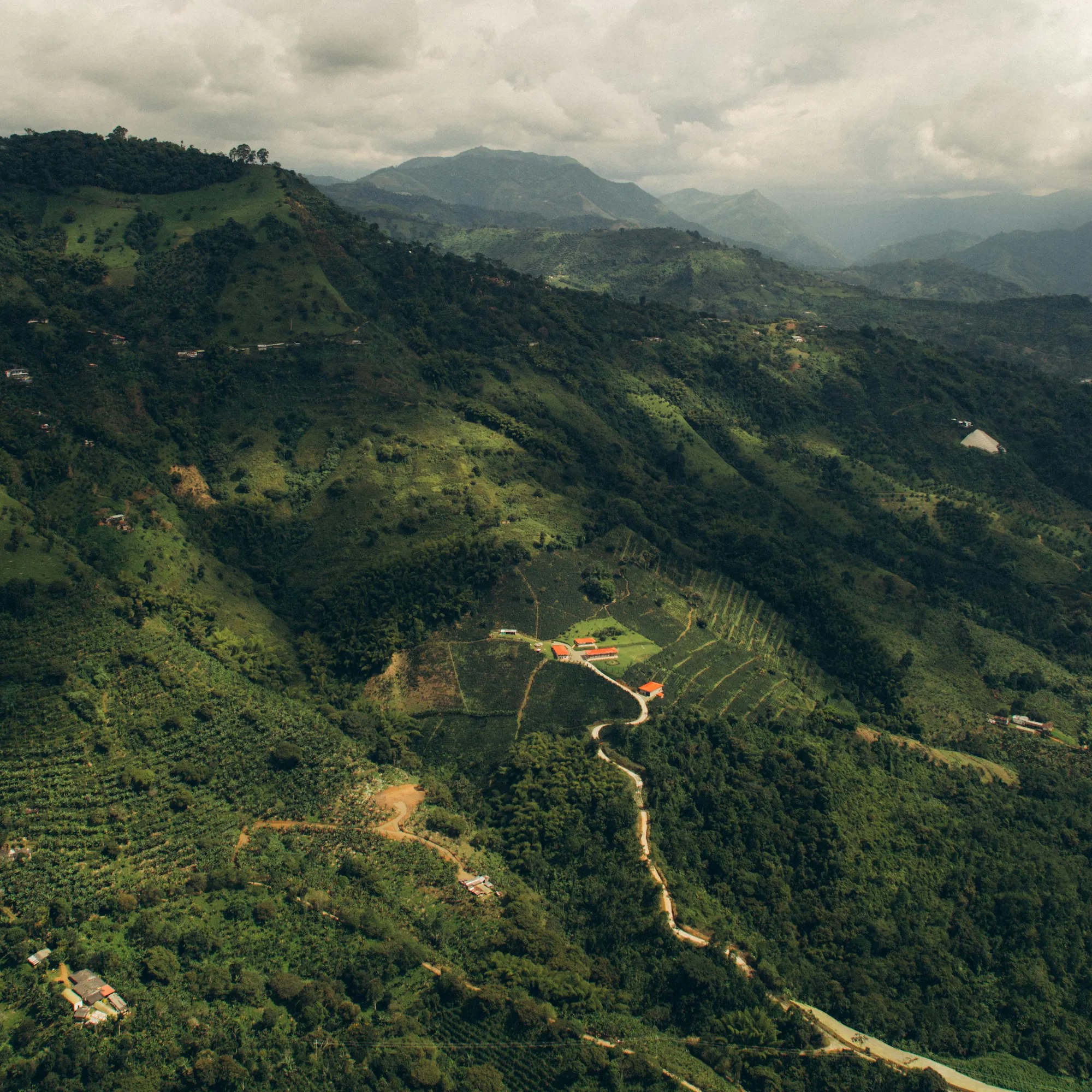 A lush green Colombian mountain valley with forested ridges recedes under overcast skies.