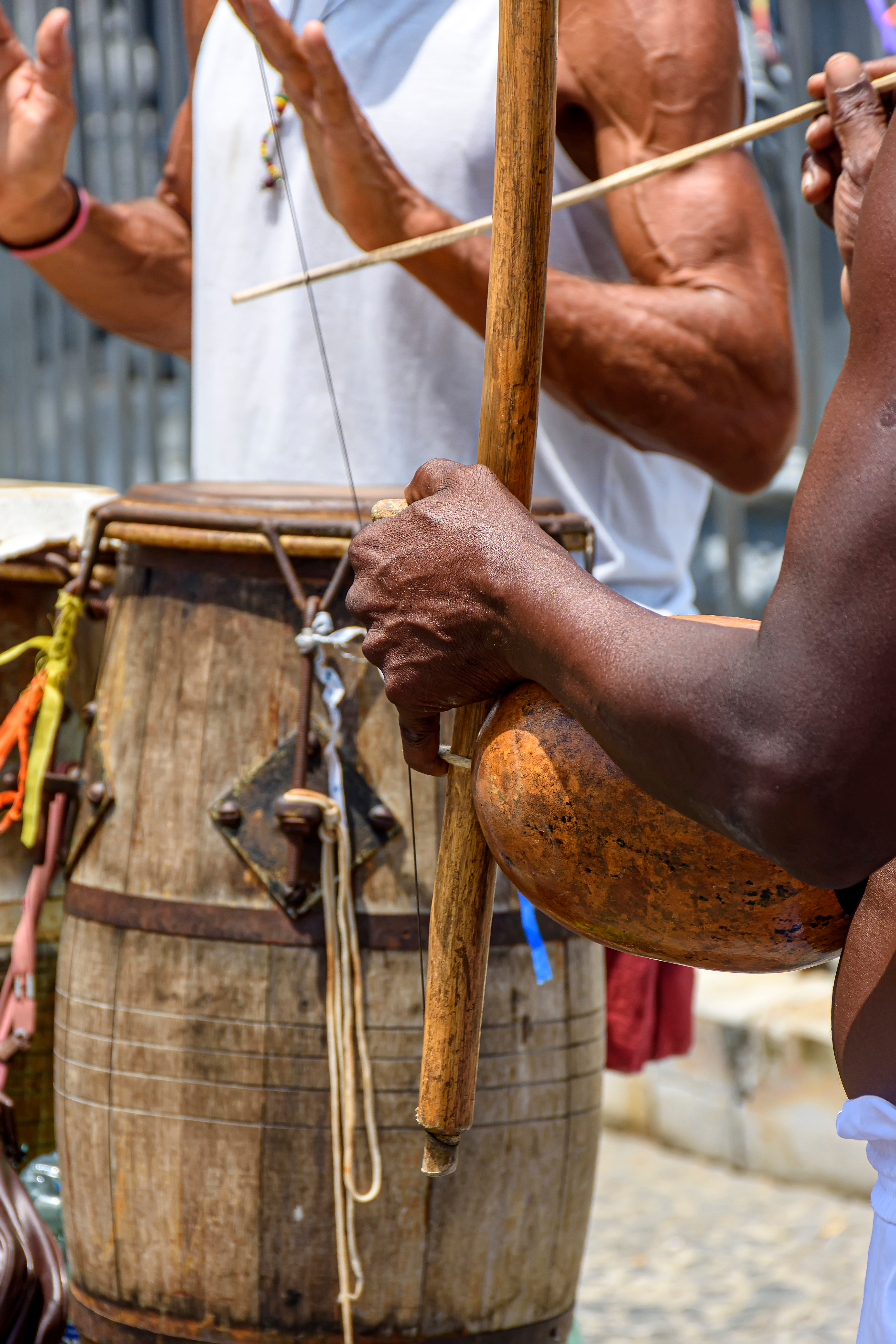 A person plays a traditional berimbau instrument on a sunlit terrace in Salvador, Bahia.