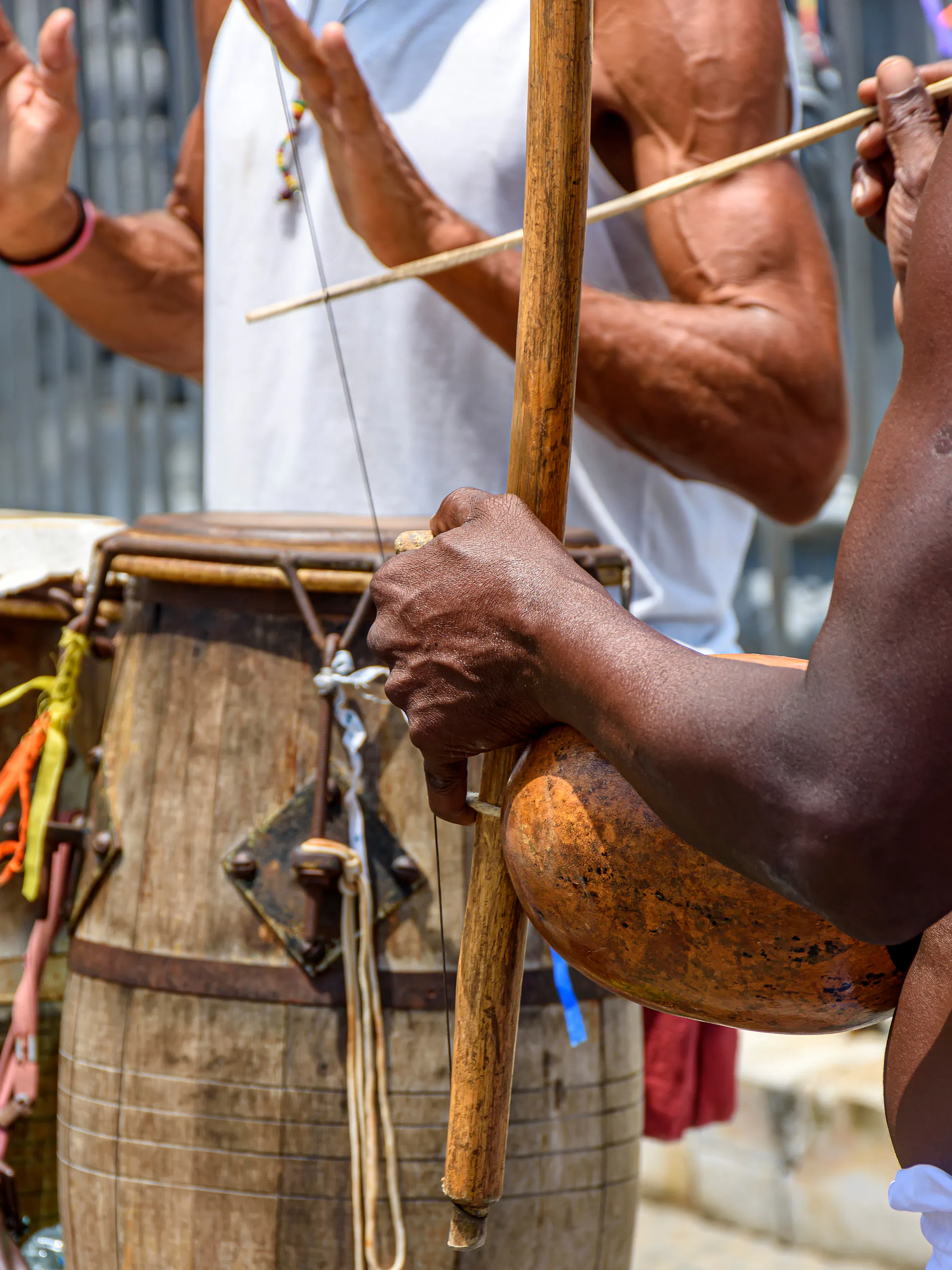 A person plays a traditional berimbau instrument on a sunlit terrace in Salvador, Bahia.