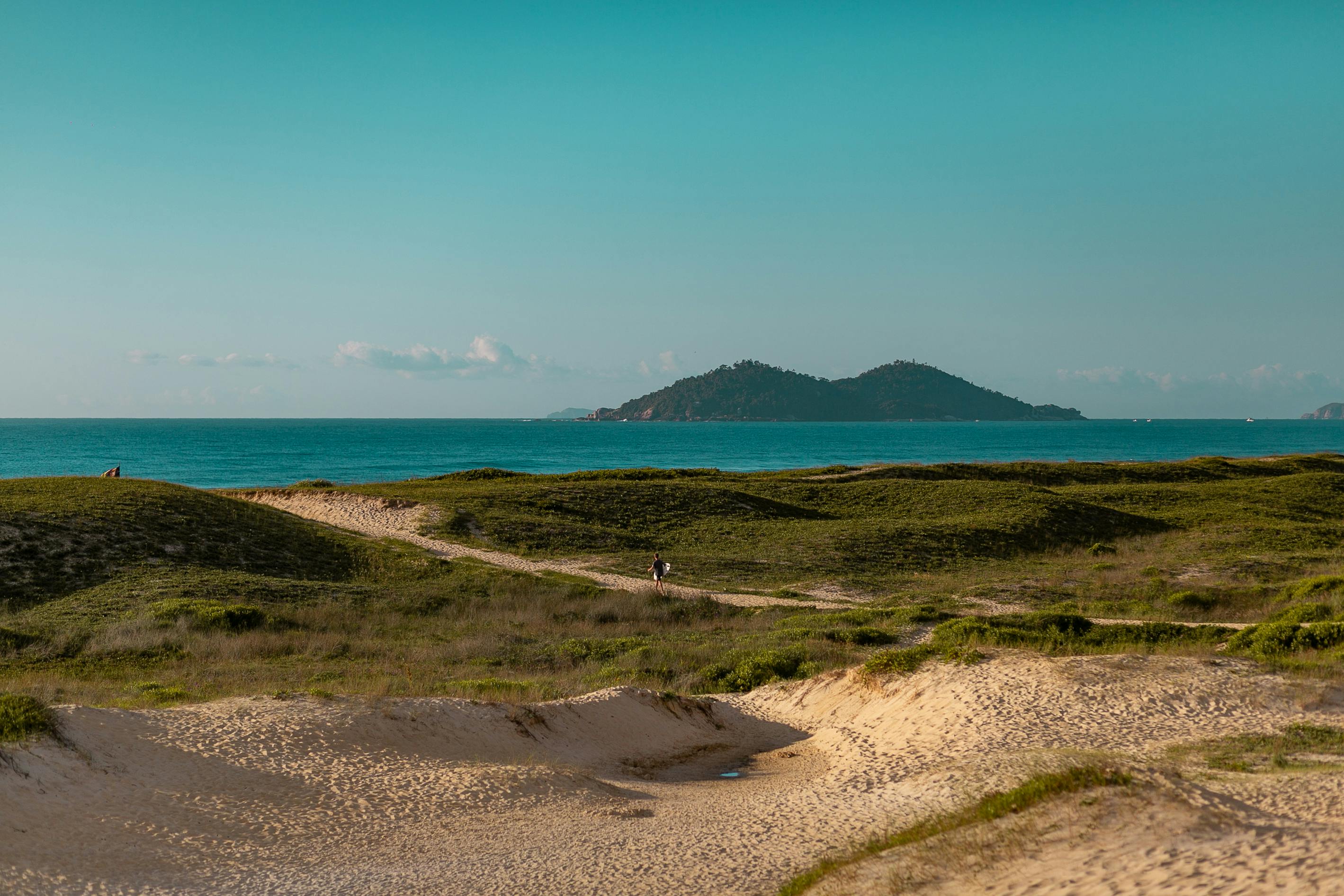 A flat sandy island with sparse low shrubs sits in a wide shallow lagoon in Florianópolis.