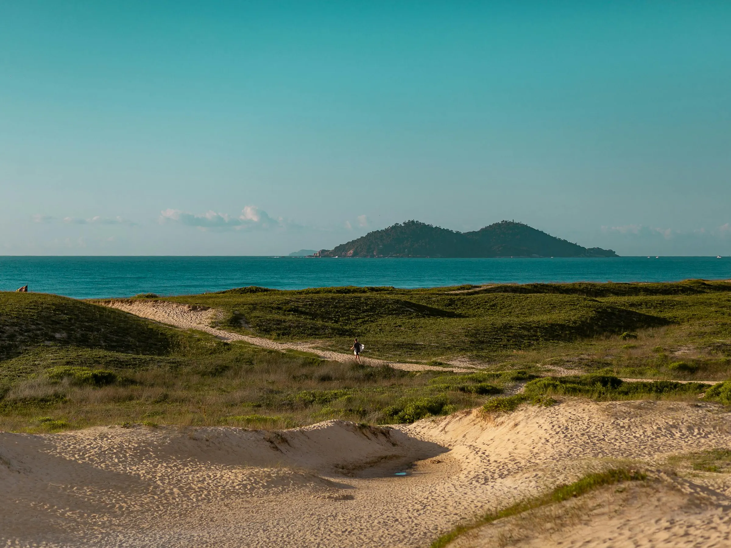 A flat sandy island with sparse low shrubs sits in a wide shallow lagoon in Florianópolis.