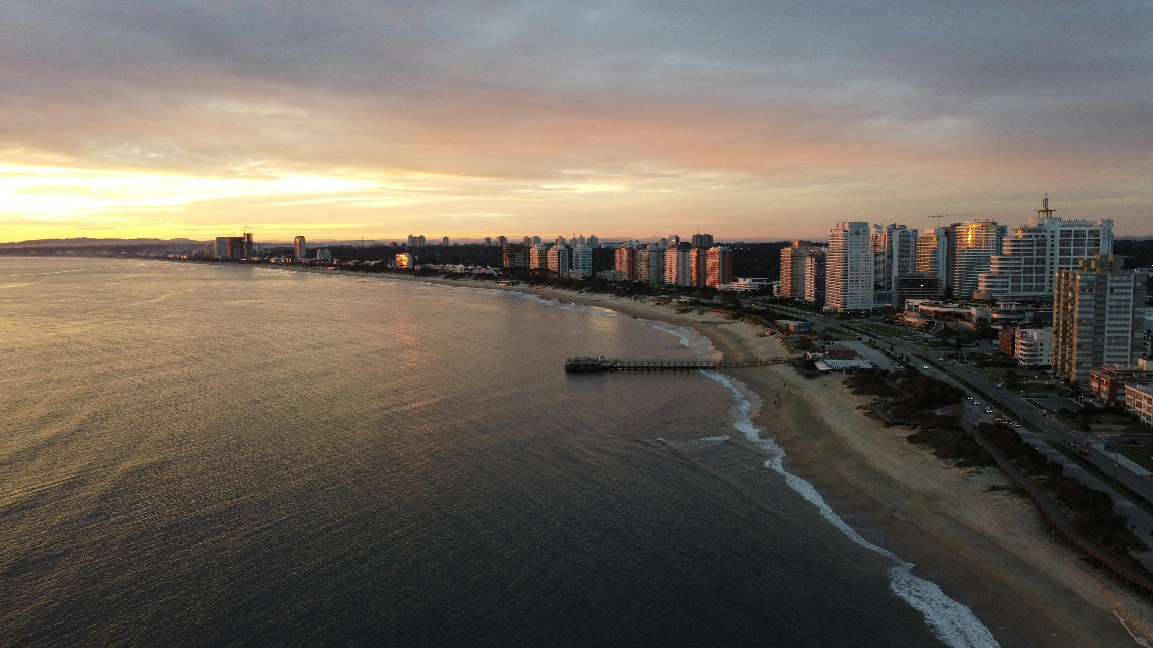 City lights reflect in calm water at dusk as Punta del Este's skyline glows on the horizon.