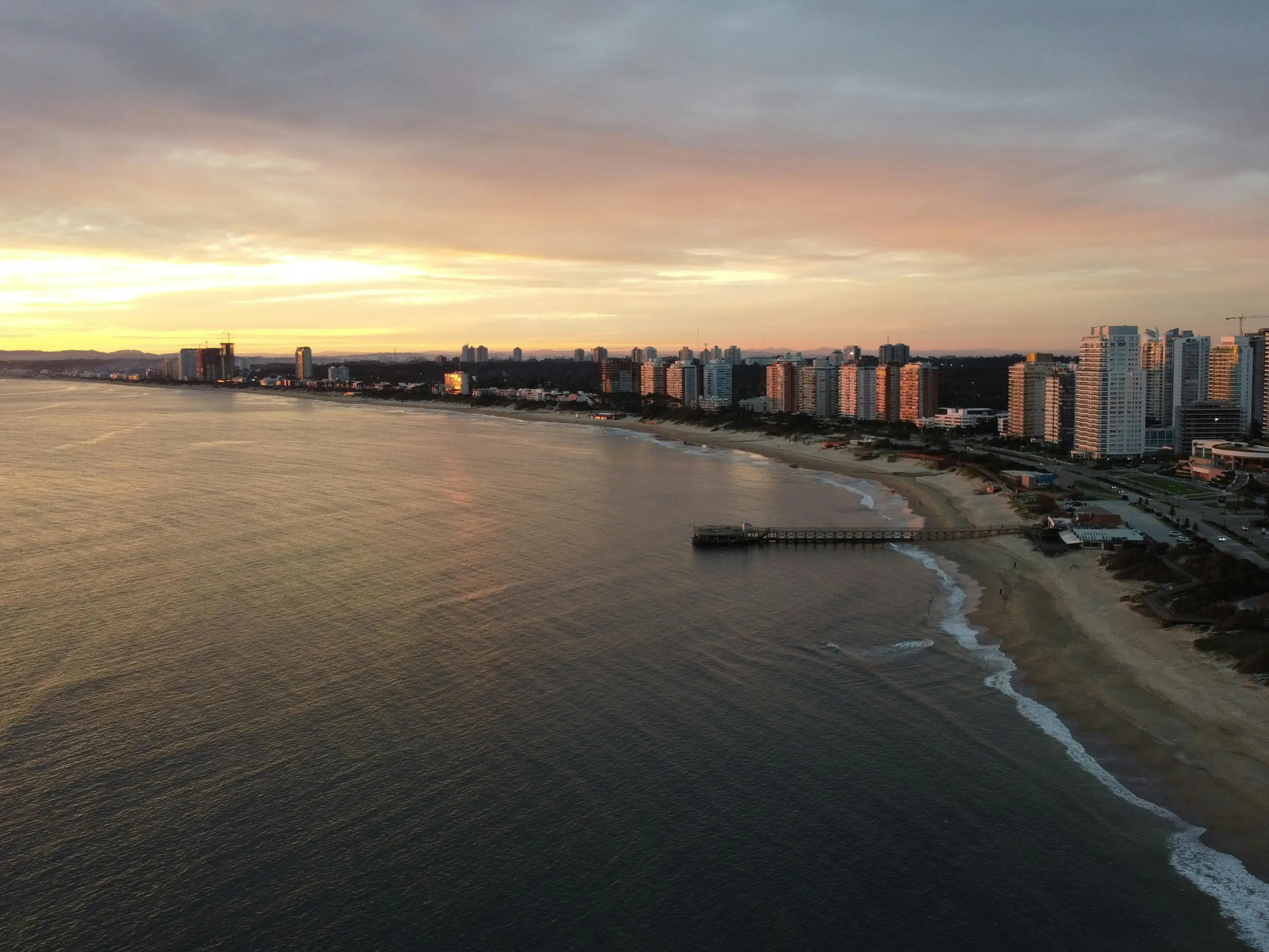 City lights reflect in calm water at dusk as Punta del Este's skyline glows on the horizon.