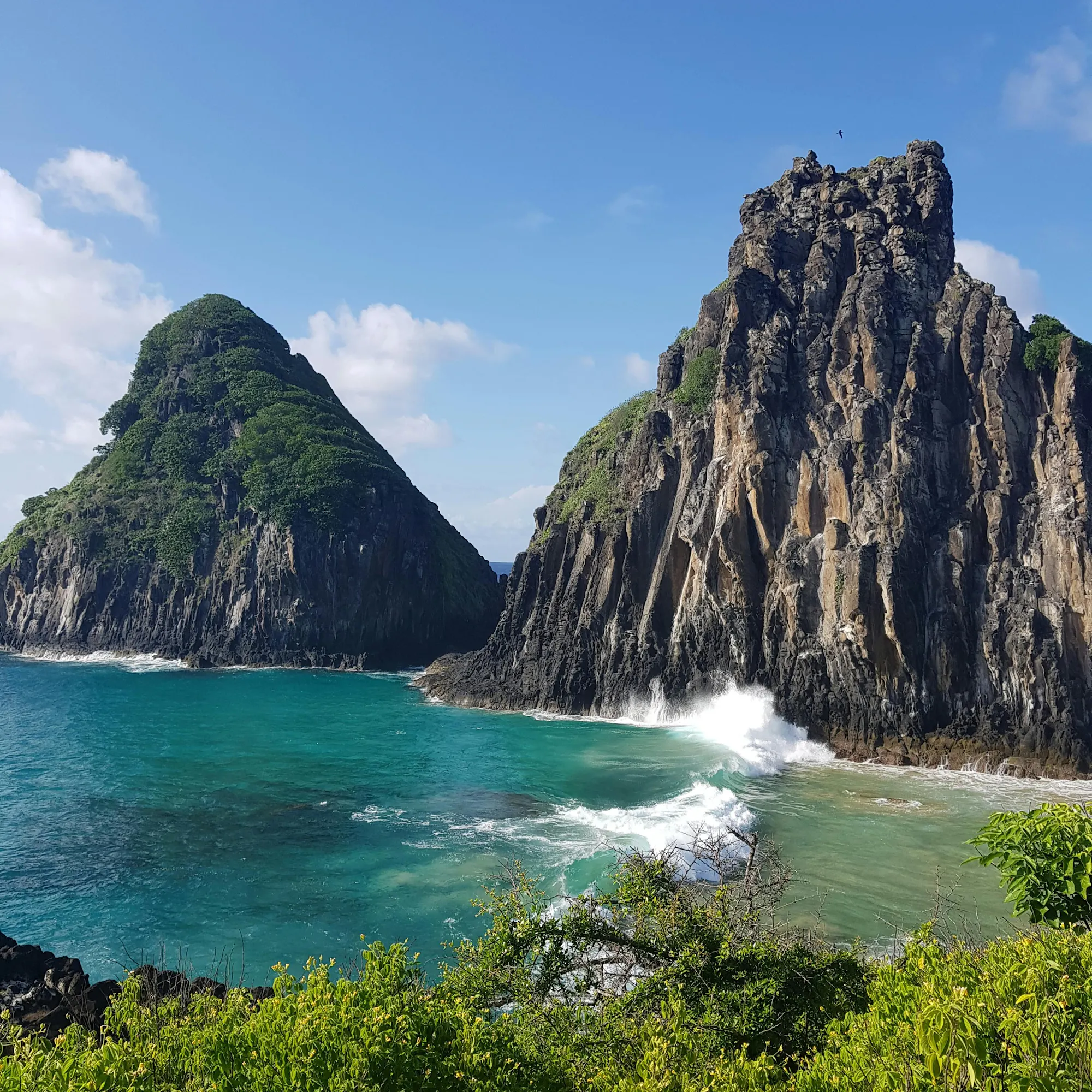 A dramatic twin-peaked volcanic rock formation rises from the ocean off Fernando de Noronha.