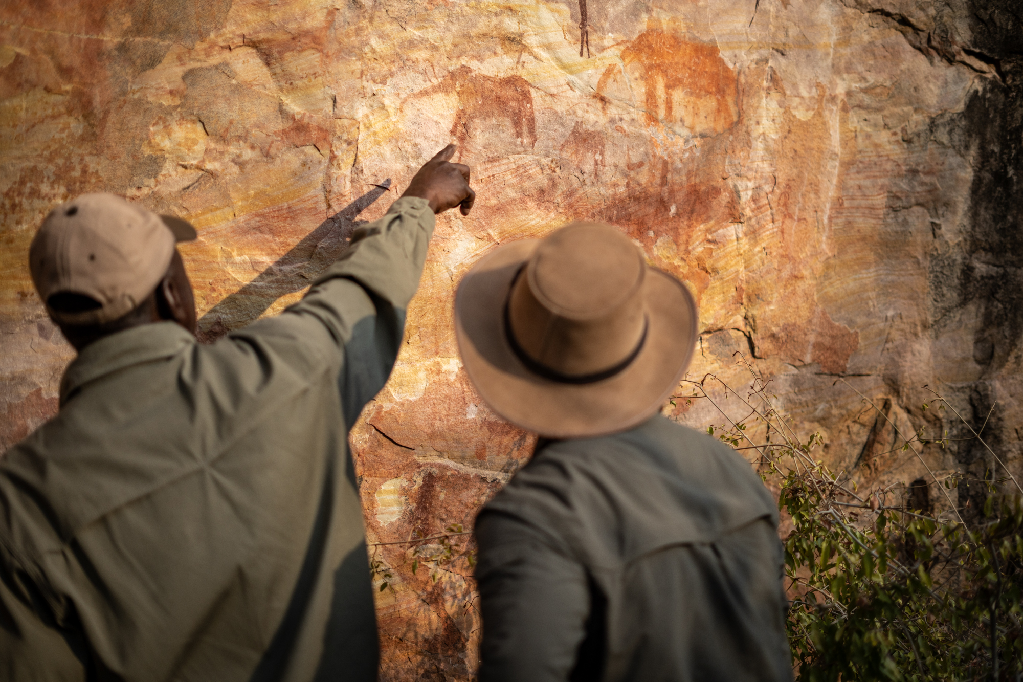 A guide points at ancient ochre rock art figures painted on a stone overhang in Zimbabwe.
