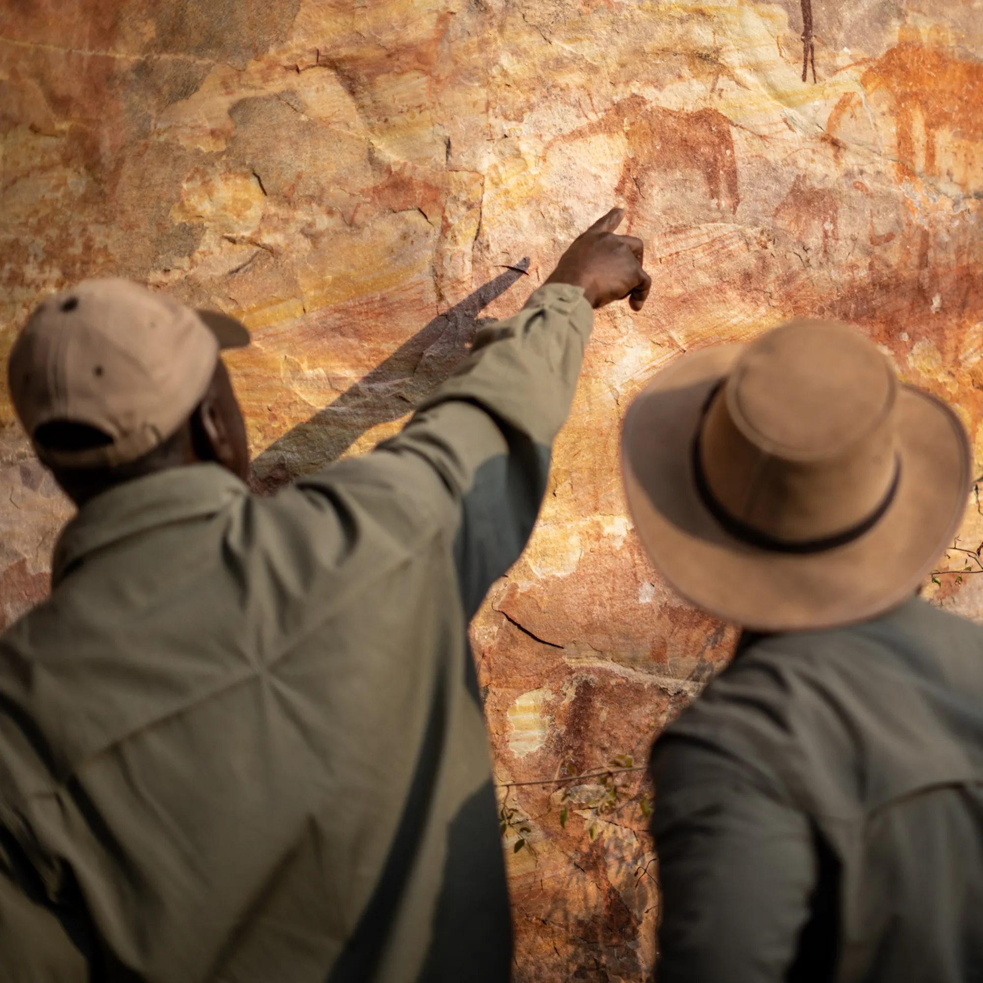 A guide points at ancient ochre rock art figures painted on a stone overhang in Zimbabwe.