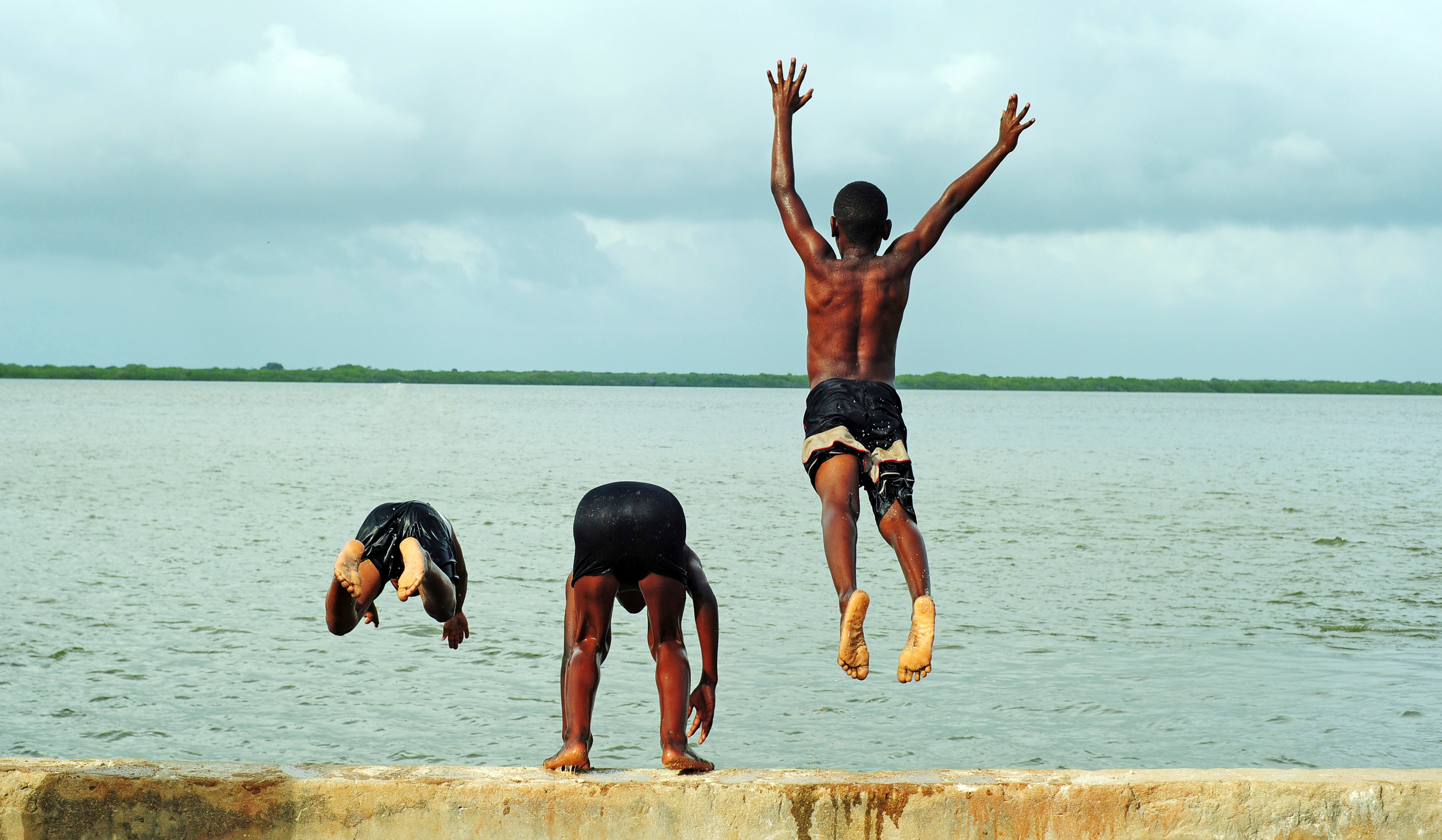 Two people jump in the air on a bright white sand beach with turquoise ocean behind them.