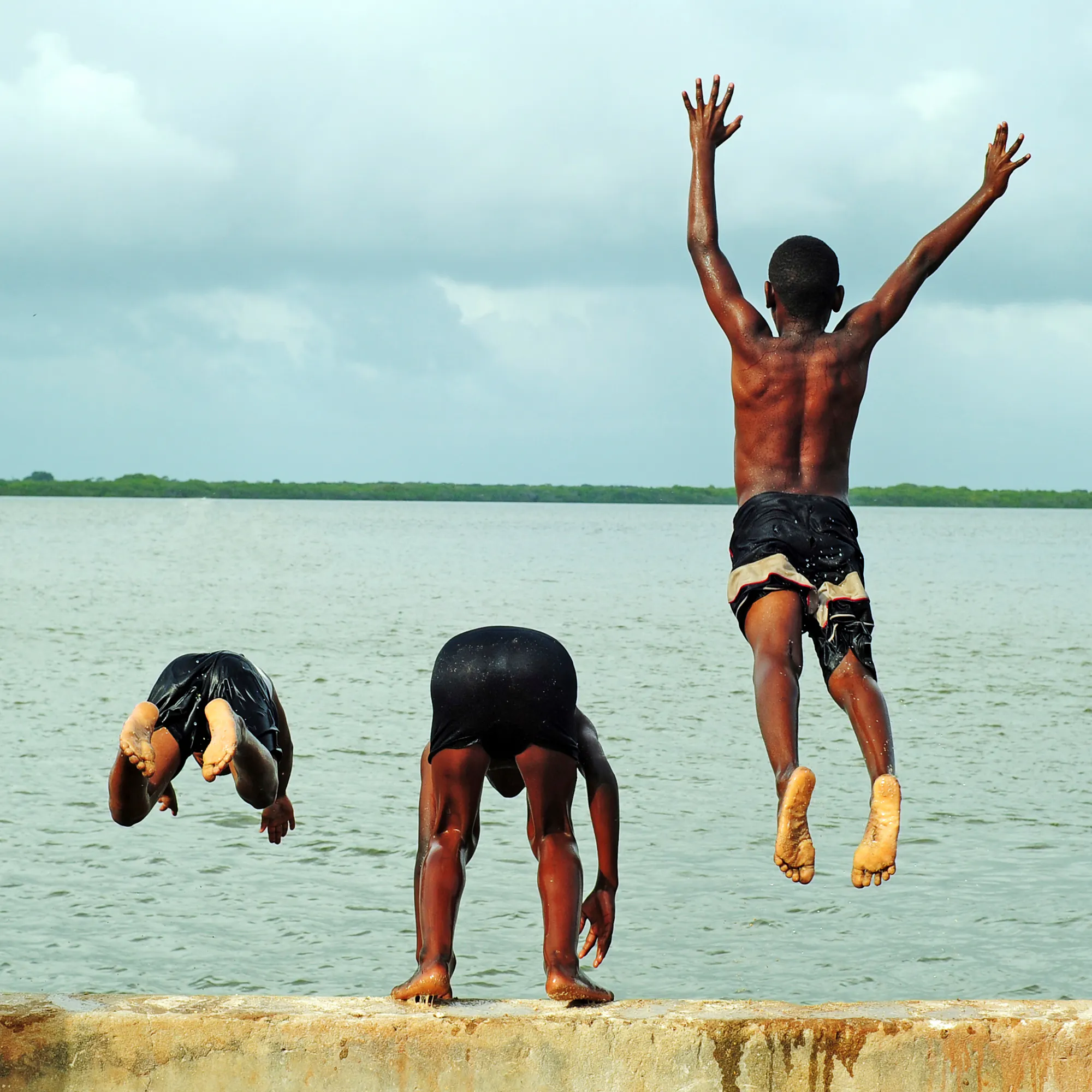 Two people jump in the air on a bright white sand beach with turquoise ocean behind them.