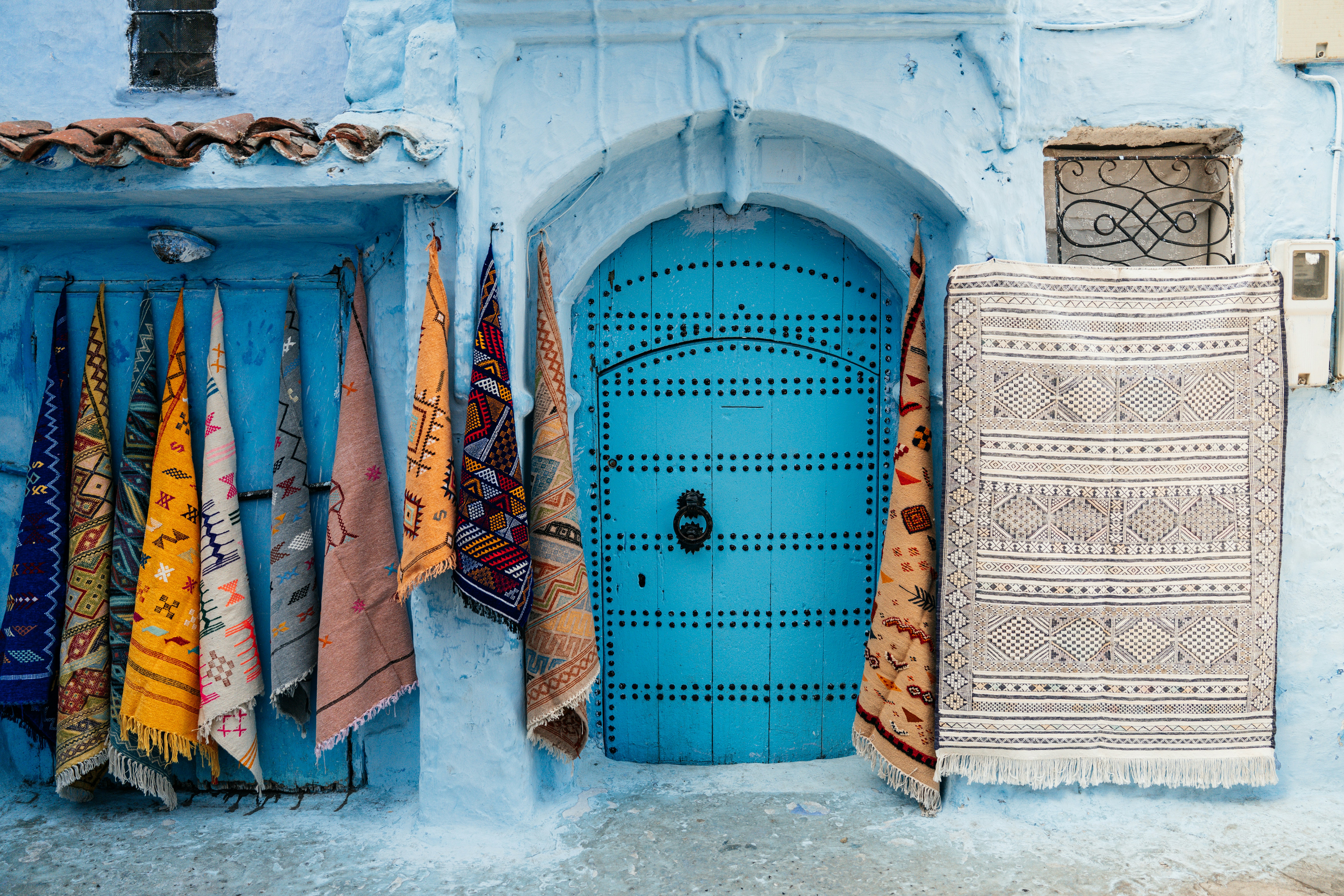 Woven textiles in vivid colors hang beside a bright blue-painted door in Chefchaouen's medina.