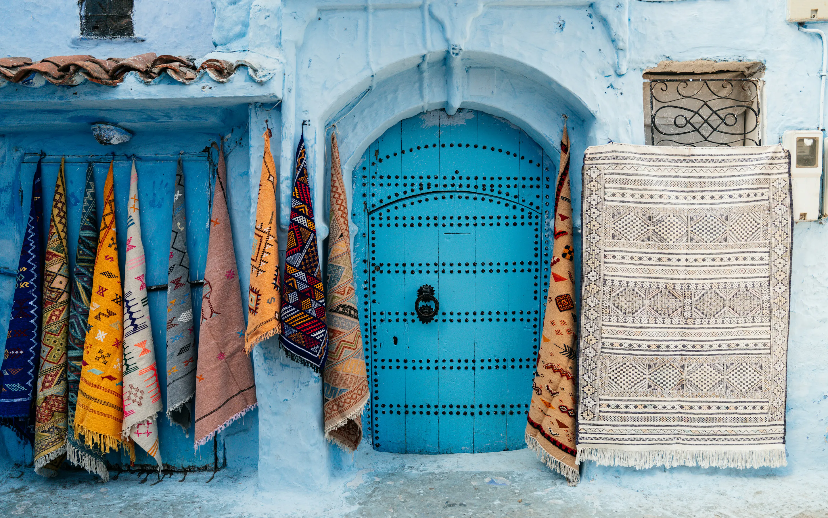 Woven textiles in vivid colors hang beside a bright blue-painted door in Chefchaouen's medina.
