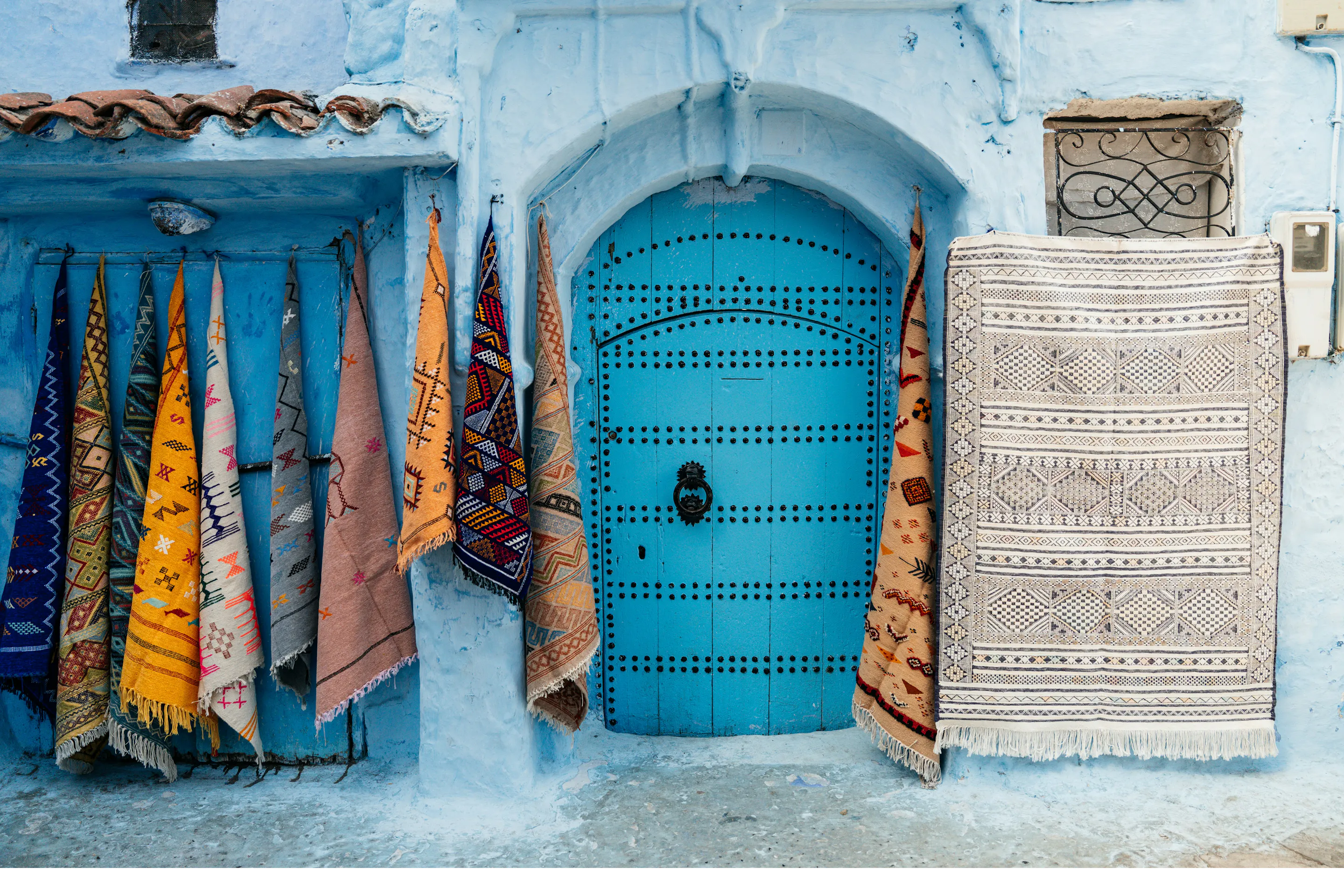 Woven textiles in vivid colors hang beside a bright blue-painted door in Chefchaouen's medina.