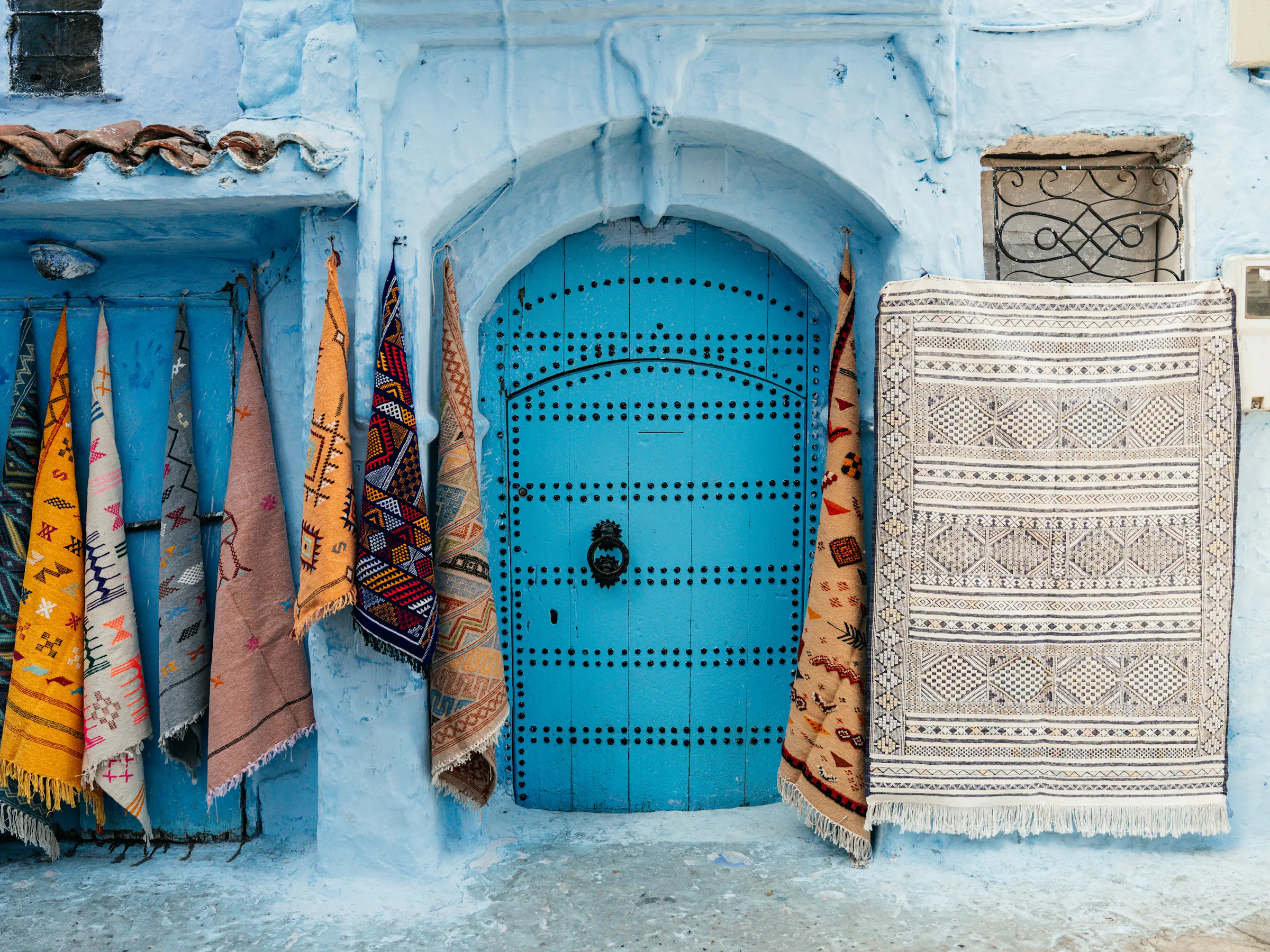 Woven textiles in vivid colors hang beside a bright blue-painted door in Chefchaouen's medina.