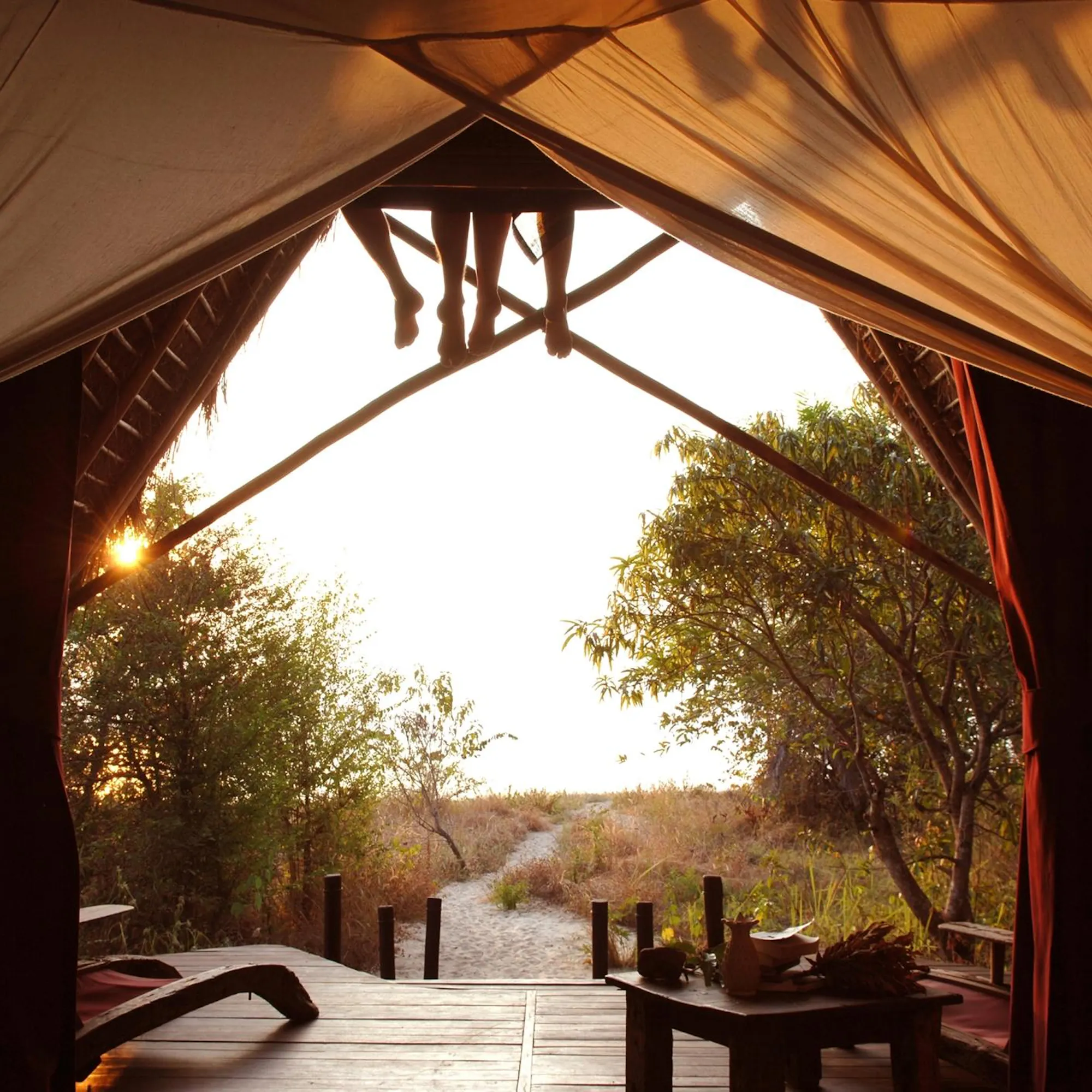 An open-sided canvas tent lodge overlooks Lake Tanganyika through palm fronds at golden hour.