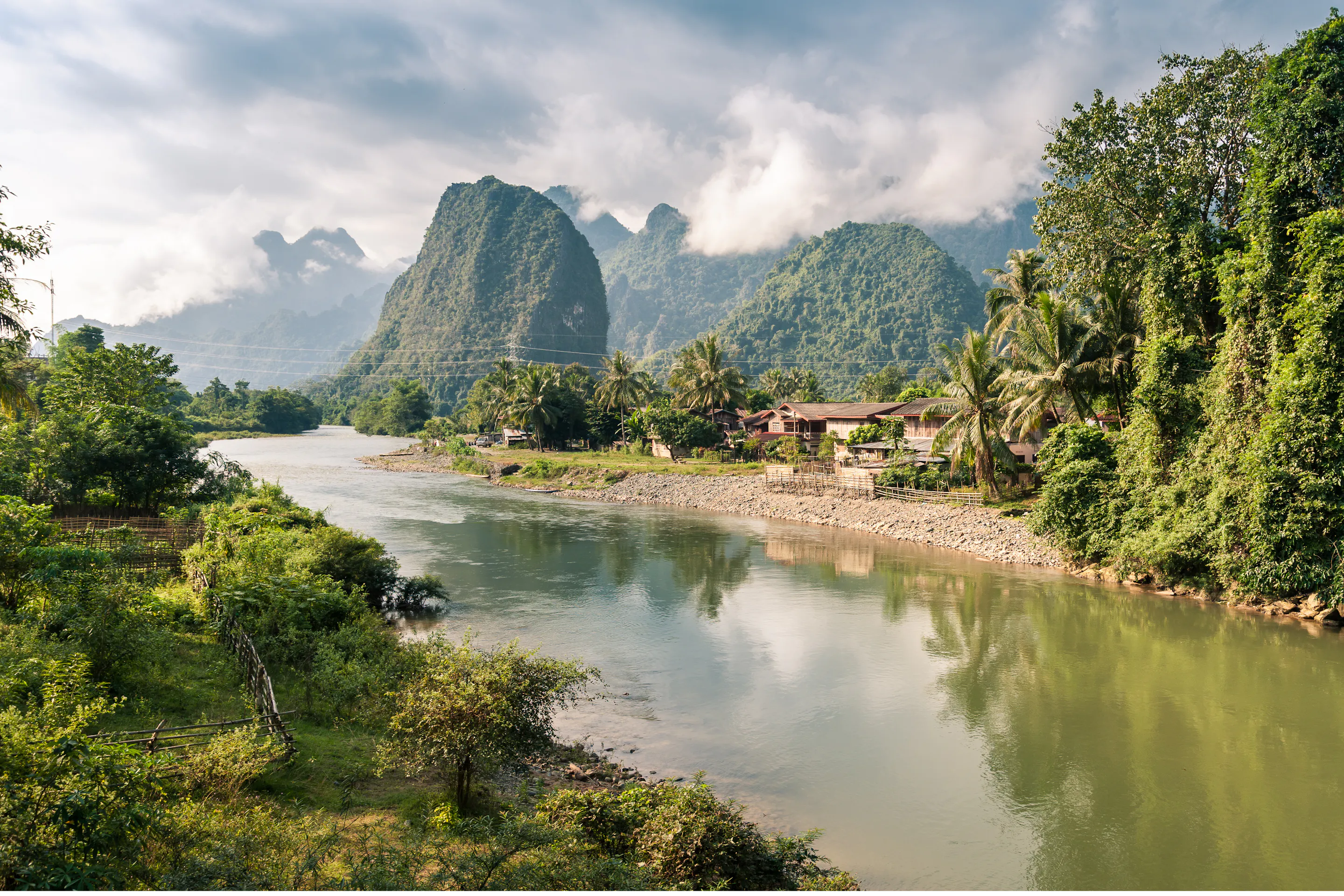 A flat green river valley is framed by dramatic karst limestone peaks in Vang Vieng, Laos.