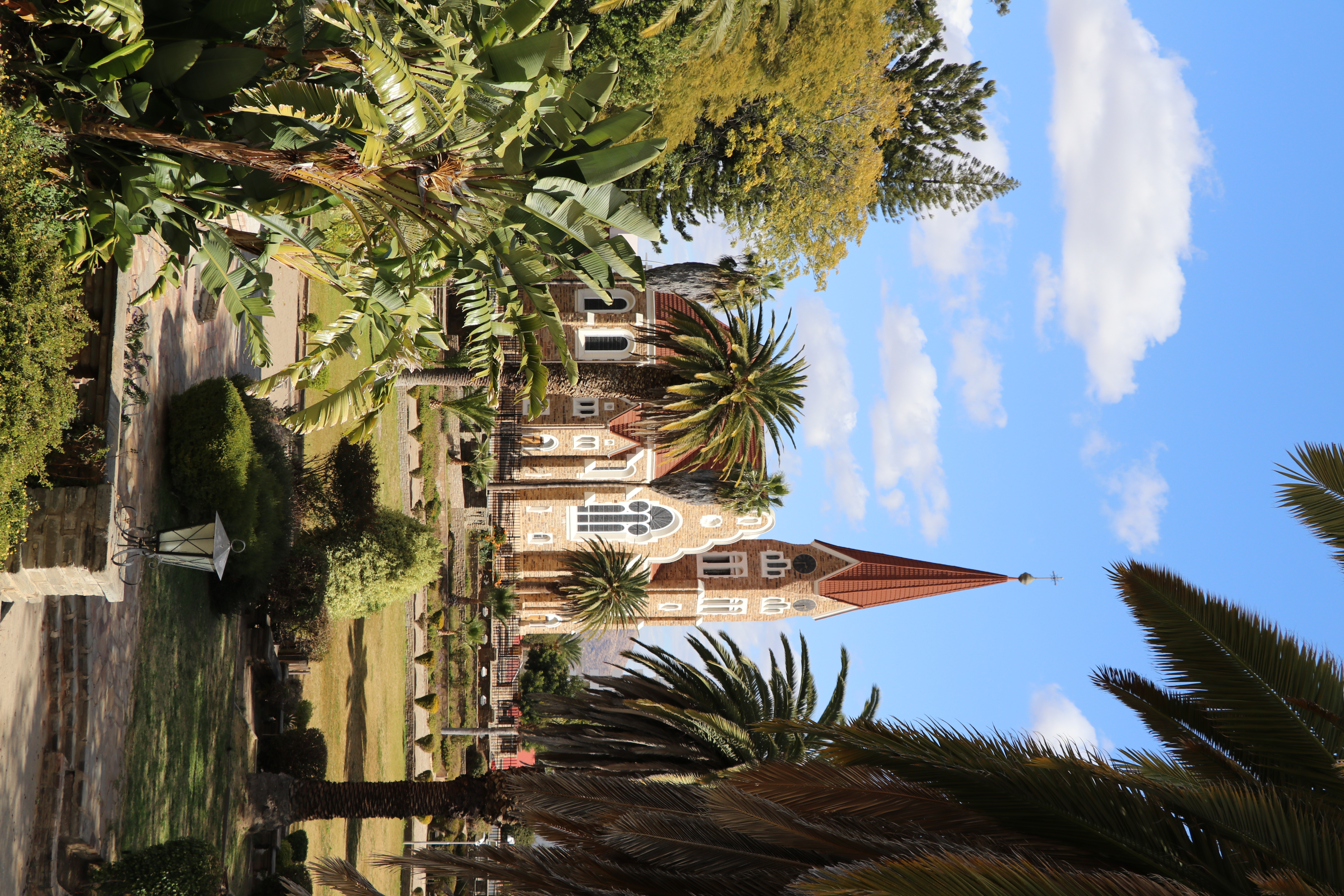A red-roofed German colonial Lutheran church rises above palm trees in central Windhoek, Namibia.