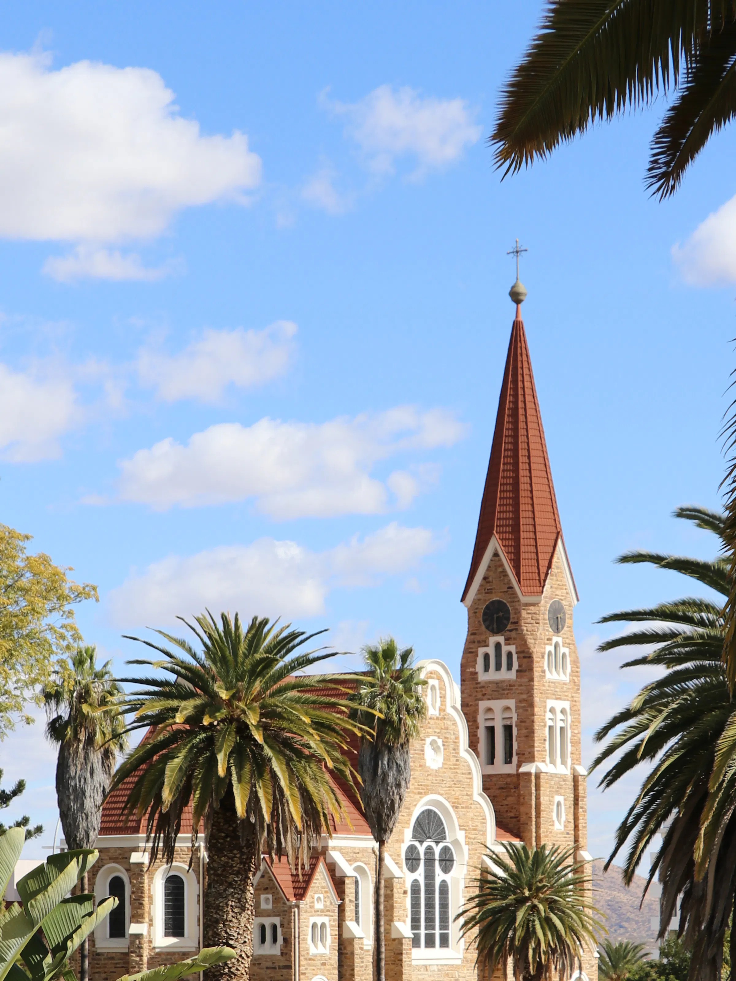 A red-roofed German colonial Lutheran church rises above palm trees in central Windhoek, Namibia.