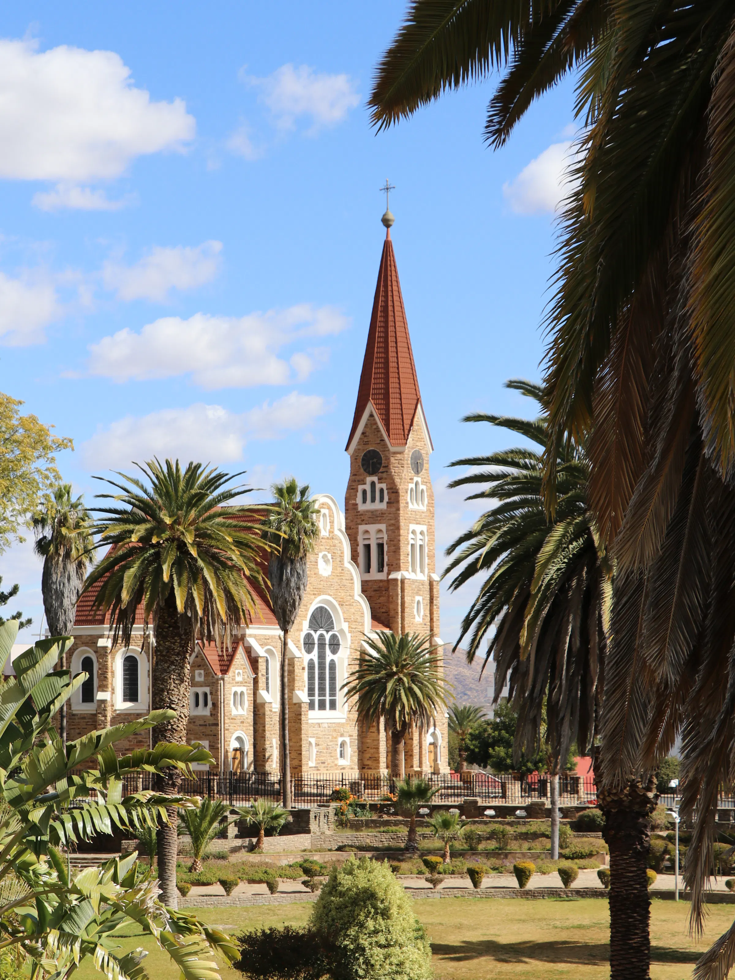A red-roofed German colonial Lutheran church rises above palm trees in central Windhoek, Namibia.