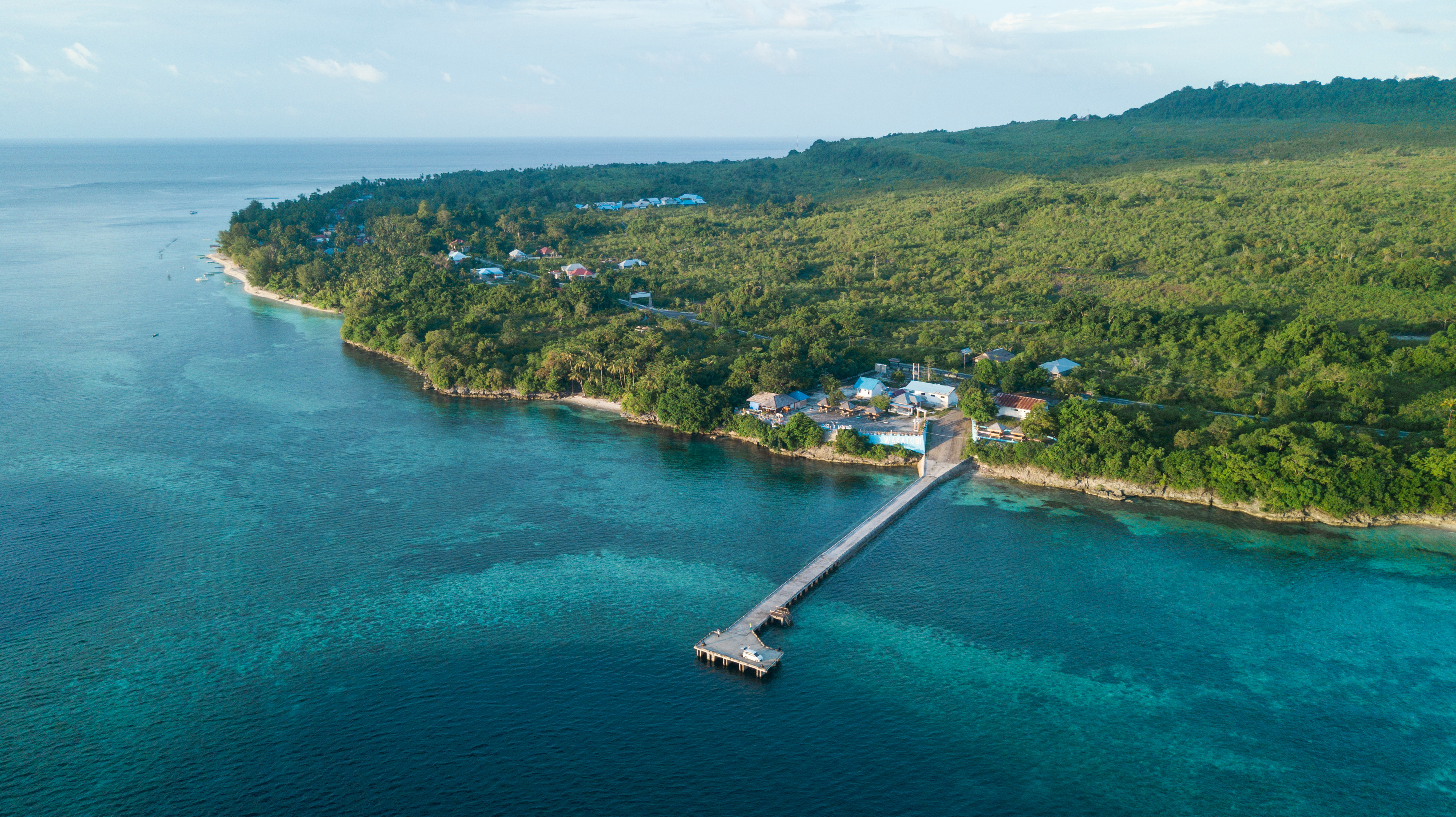 A slender wooden jetty extends over clear turquoise water in the Wakatobi archipelago, Sulawesi.