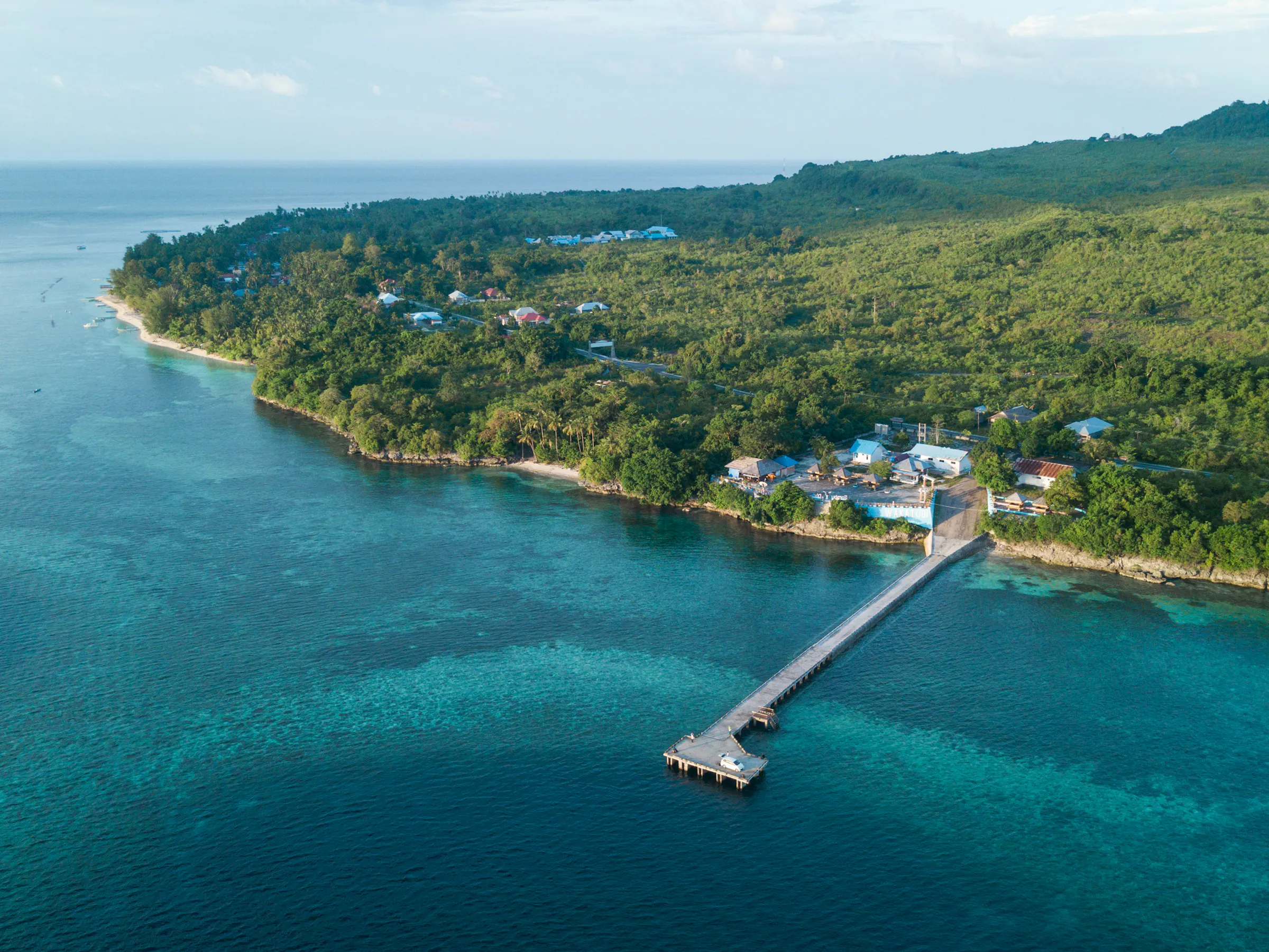 A slender wooden jetty extends over clear turquoise water in the Wakatobi archipelago, Sulawesi.