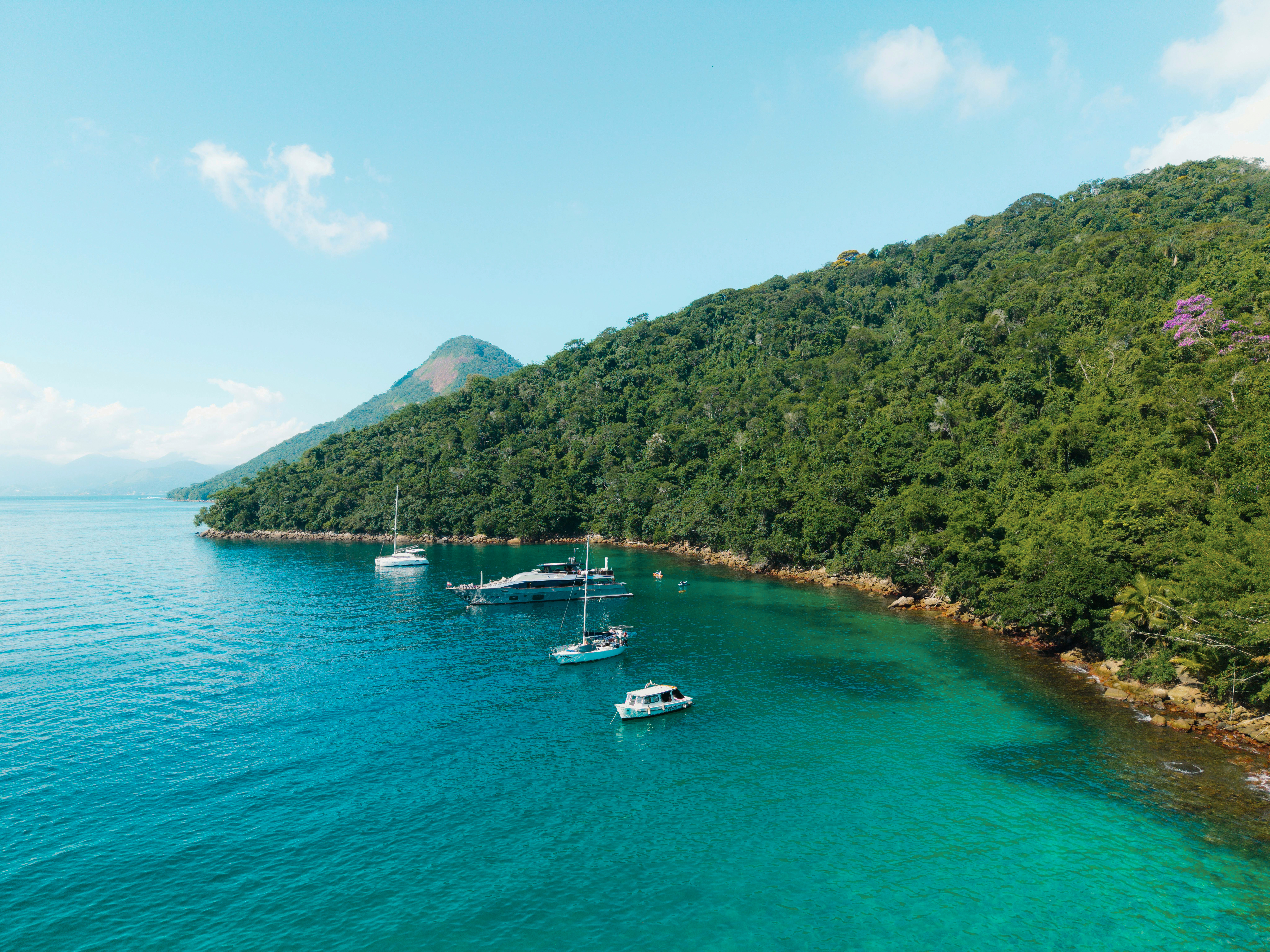 Sailboats anchor in calm turquoise water beside a densely forested green island at Ilha Grande.